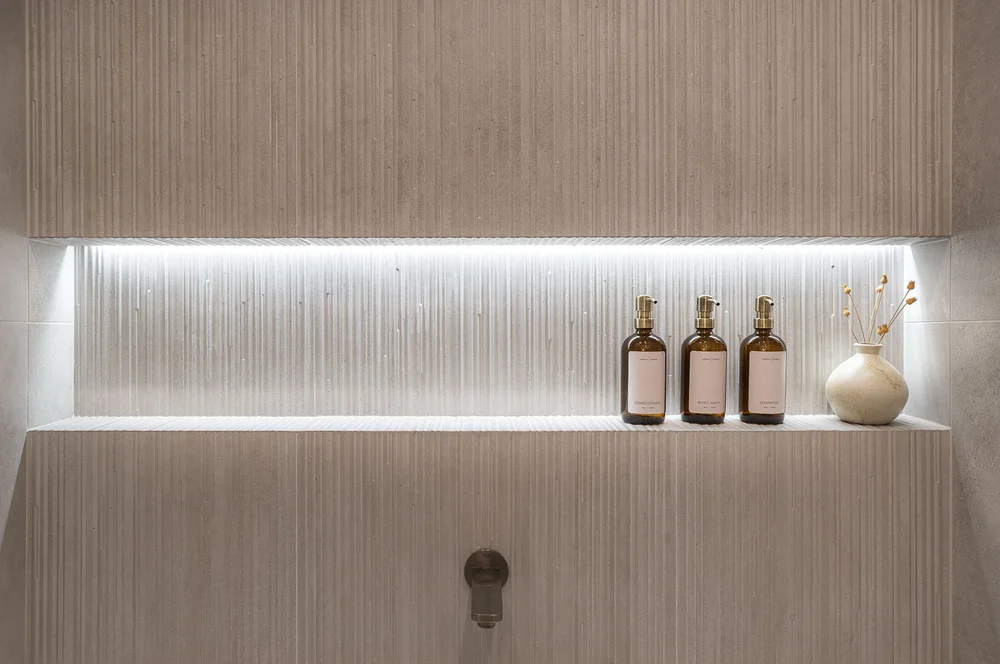 A lit recess in a ribbed wall holding three bottles and a small vase