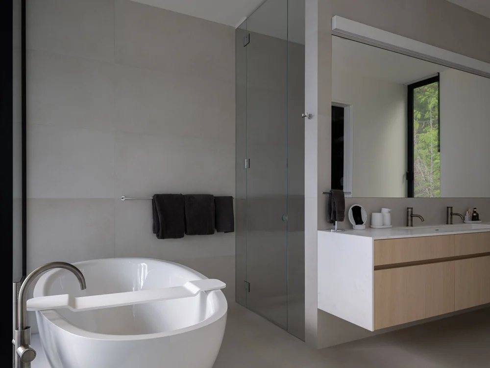 Freestanding tub beside a glass shower, dark towels on a rail and a mirrored vanity