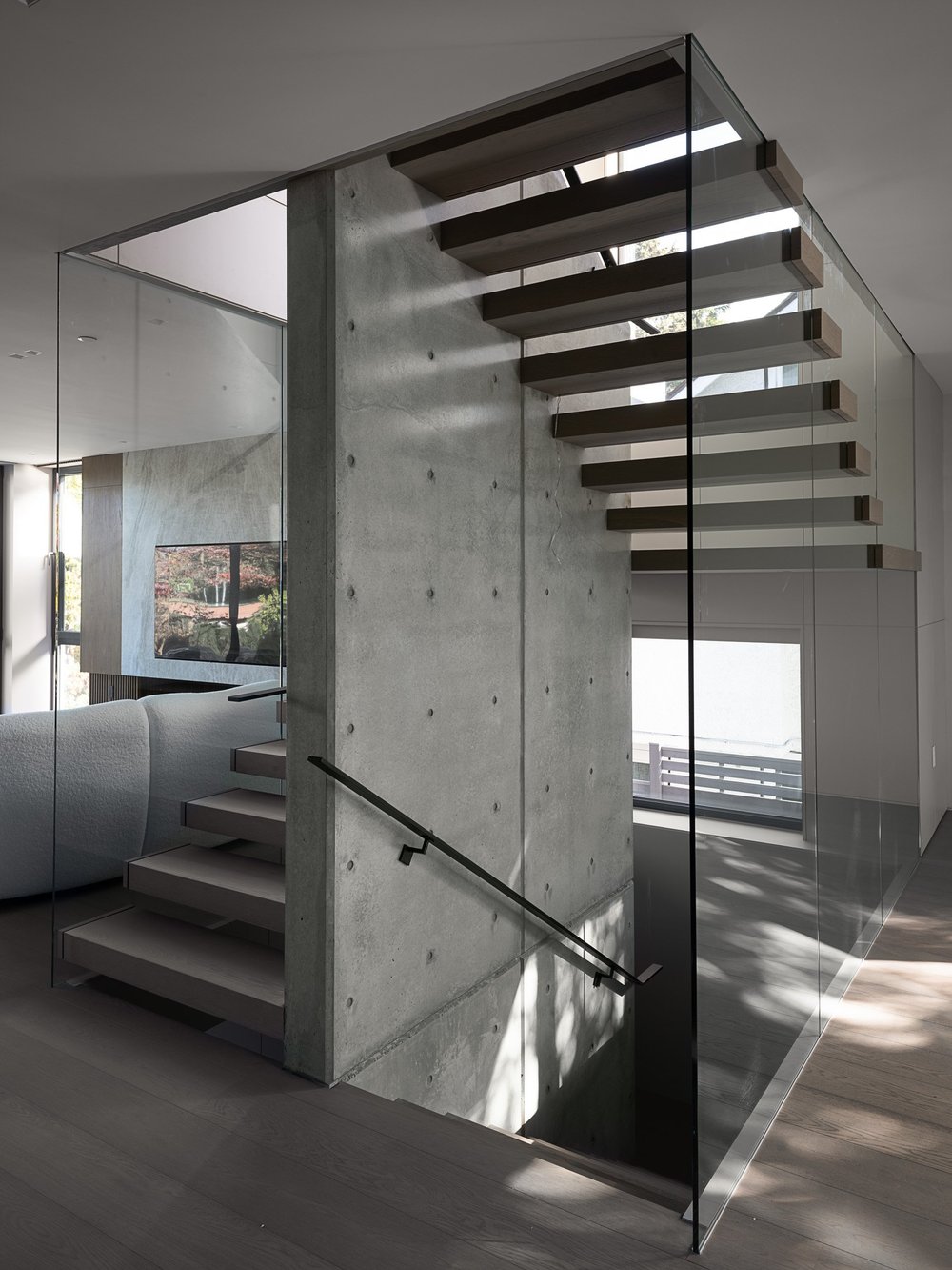 The stair against its concrete wall, glass balustrade and a slim black handrail