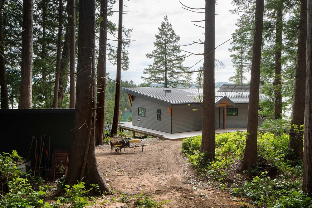 The house across a dirt clearing in the trees, a log splitter and tools nearby