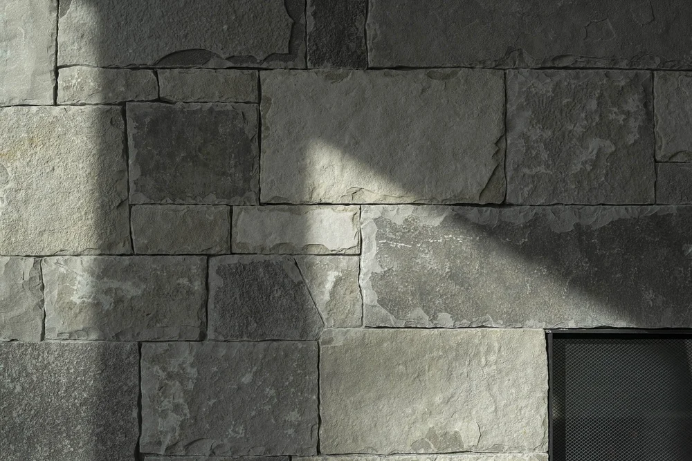Coursed stone wall in raking light, a band of sun across the blocks
