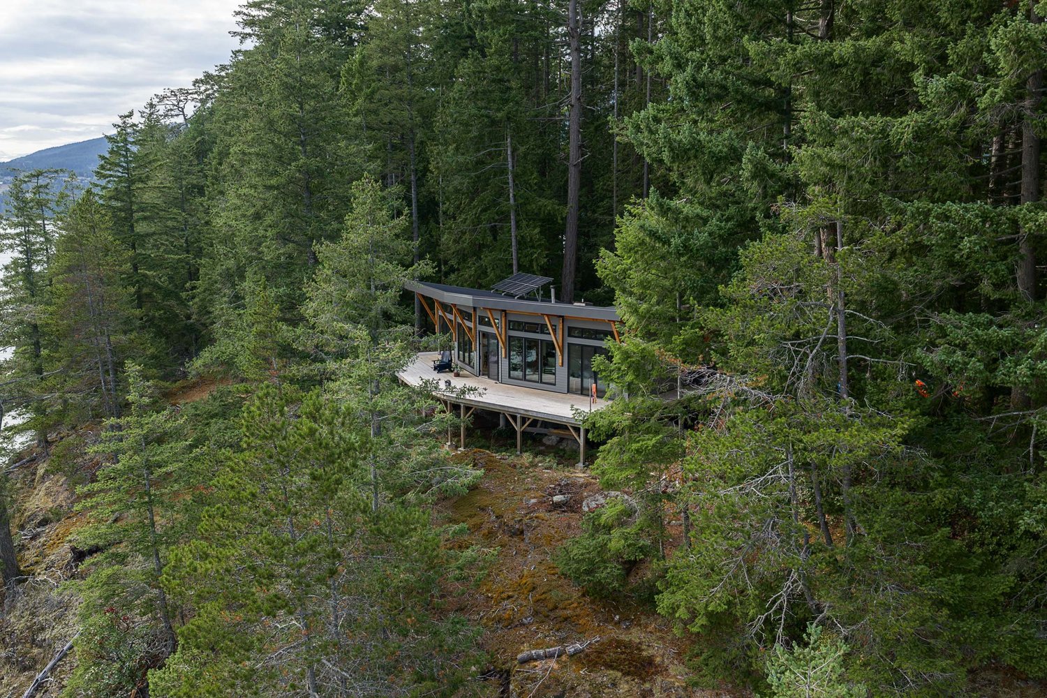 The house on a forested bluff above the water, its deck at the edge of the trees