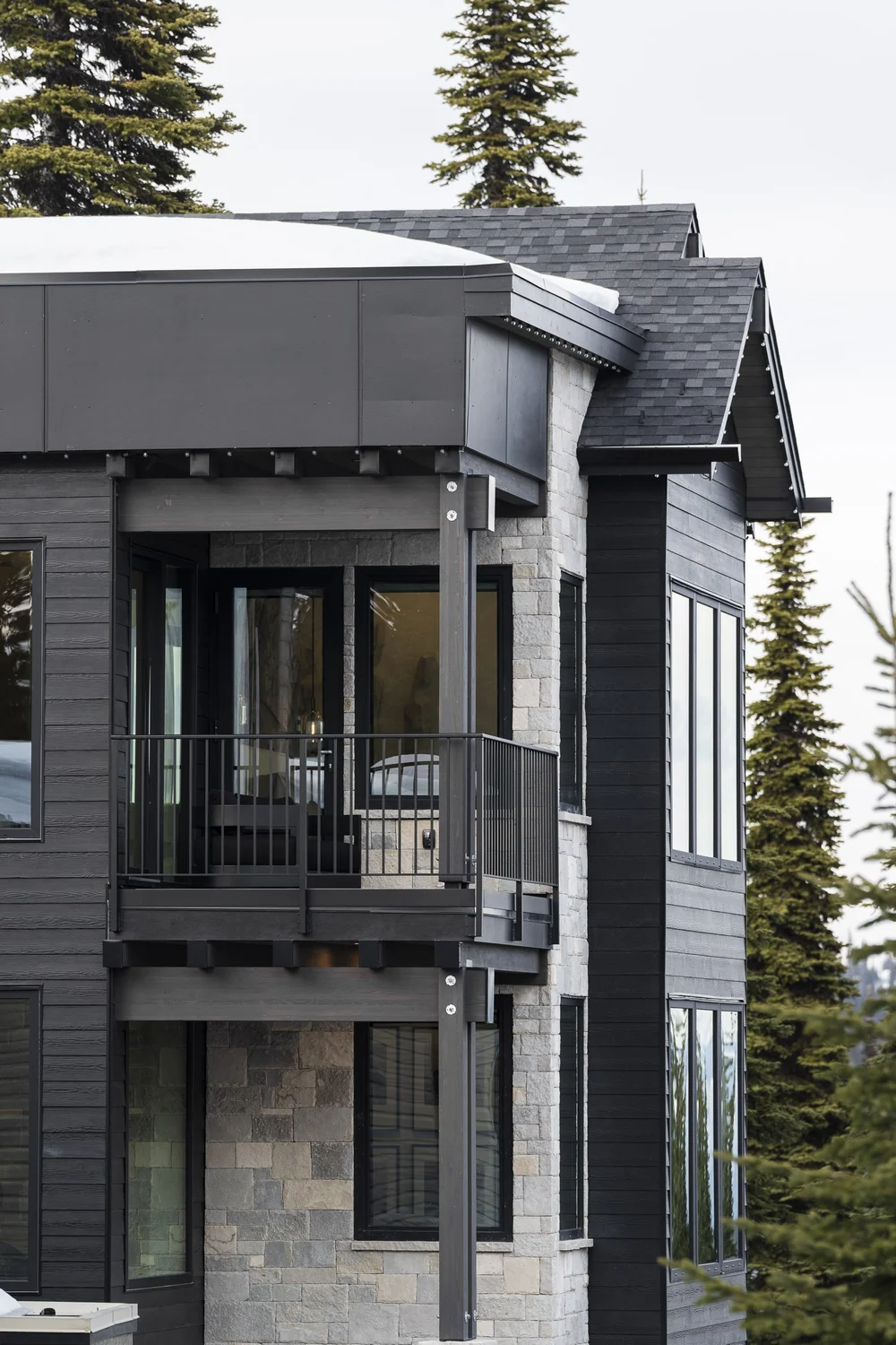 Corner of the house, stone base under dark siding with a covered balcony above