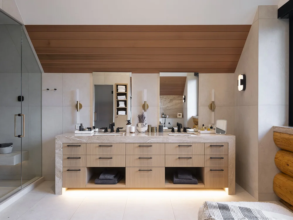 Double vanity centred under a wood plank ceiling, three sconces along a full width mirror