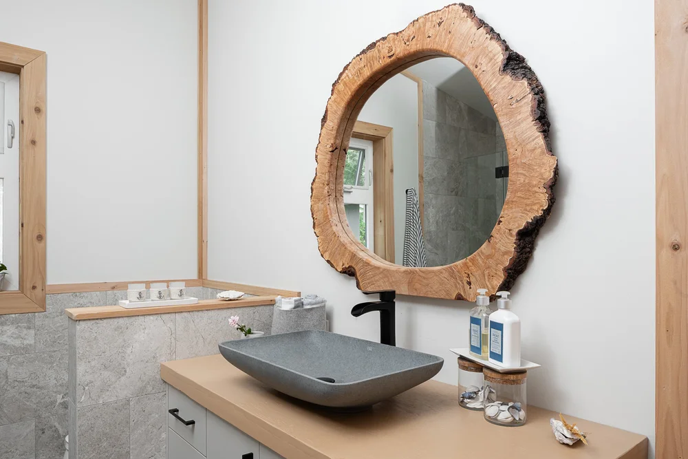 A round mirror in a live edge wood frame above a grey vessel basin