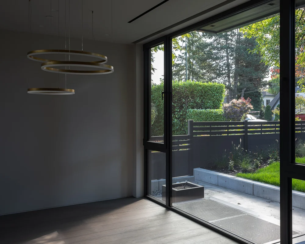 Ring pendant lights above an empty floor, sliding glass to a sunken patio and hedge