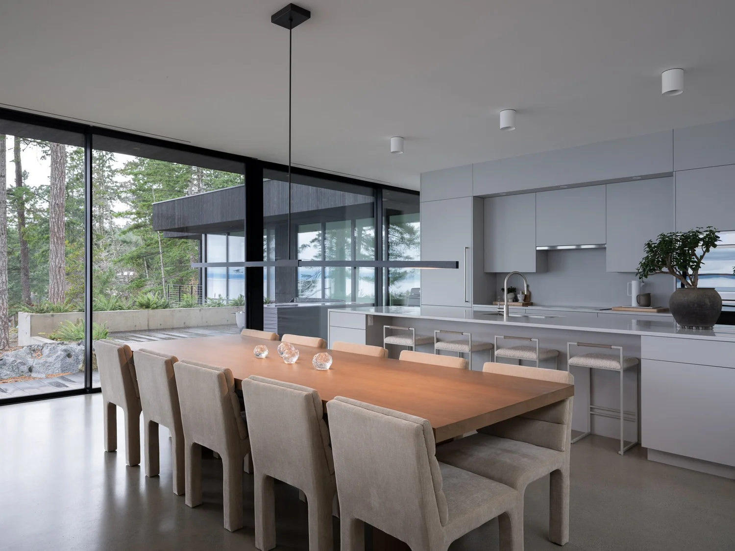 Dining table and chairs with the kitchen behind, sliding glass open to the forest