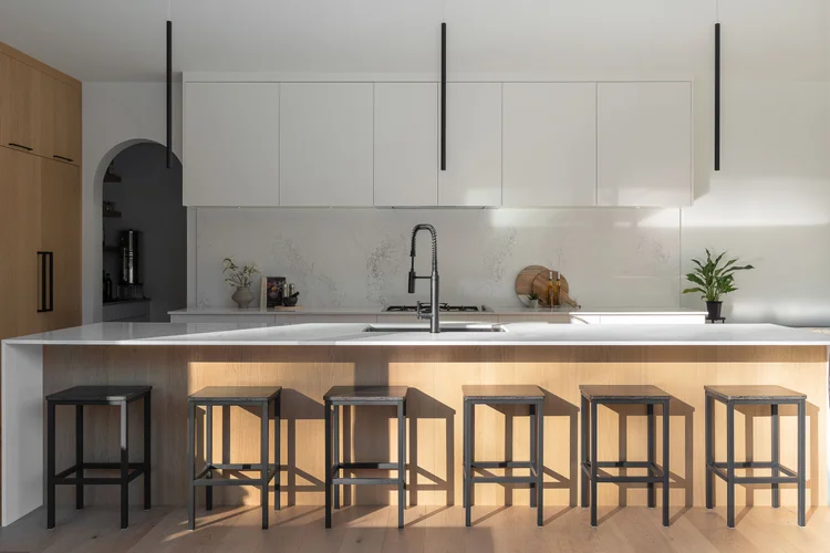 Kitchen island with six stools under slim pendants, oak and white cabinetry