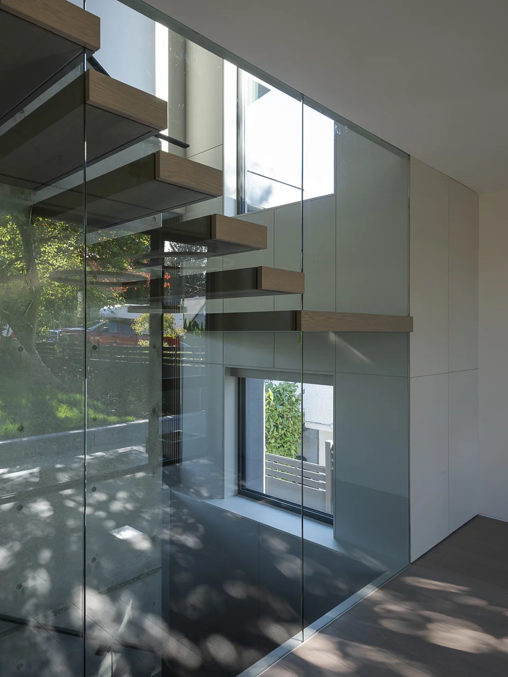 Floating stair treads read through a glass balustrade, daylight from the window wall