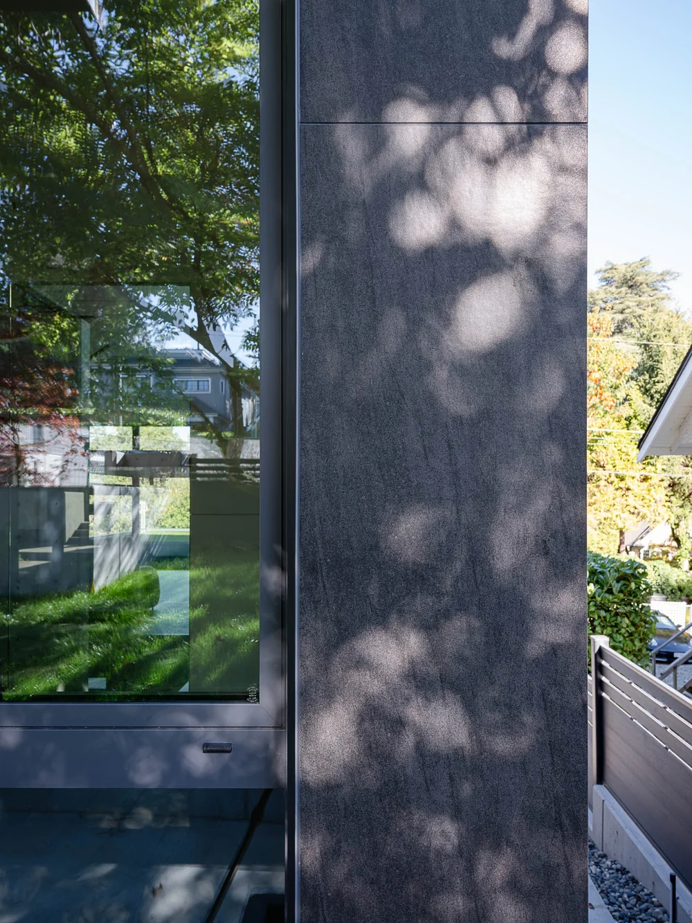 A dark clad pier beside full height glazing, tree shadows falling across it
