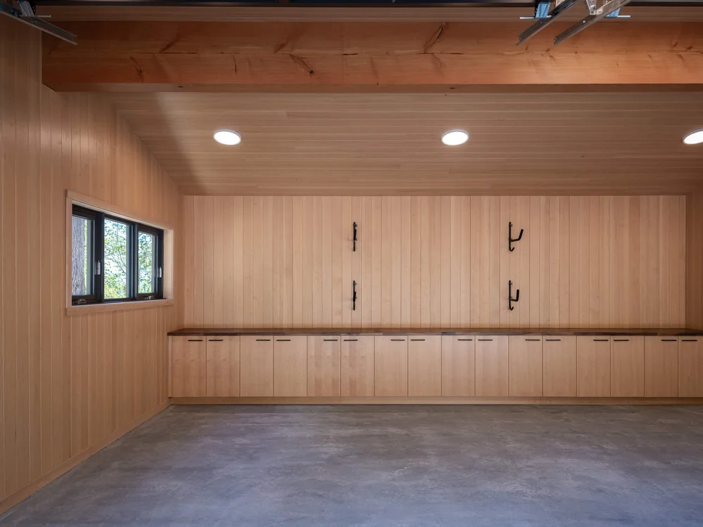 Long run of wood cabinets under a counter with wall hooks above, concrete floor
