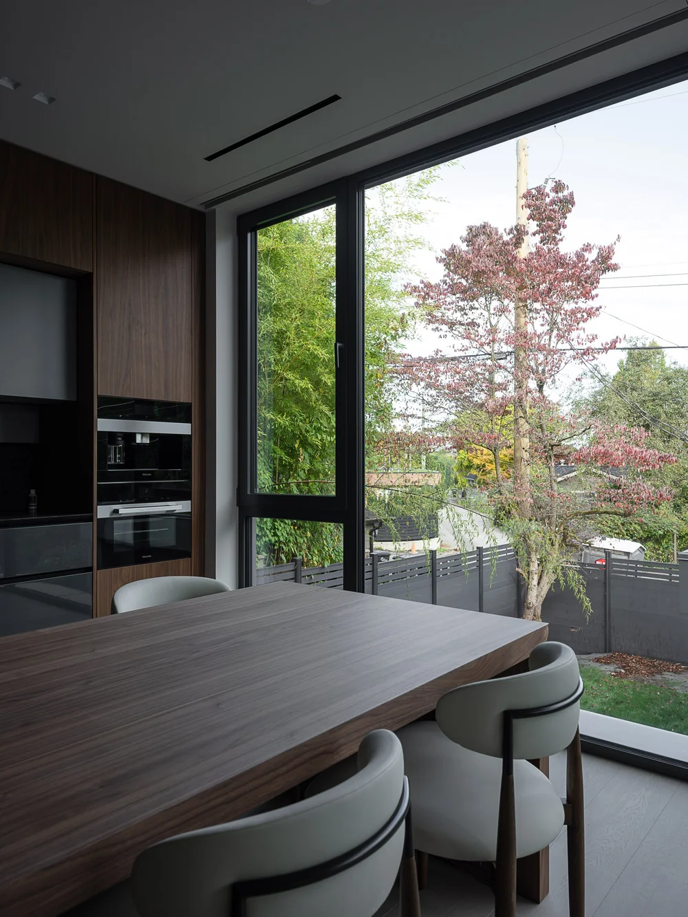 Dining chairs at a dark timber table beside glazing, a red maple outside