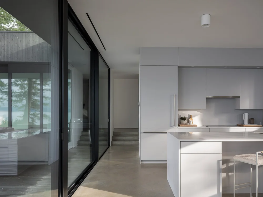 The kitchen seen past a sliding glass wall, concrete steps rising to a landing