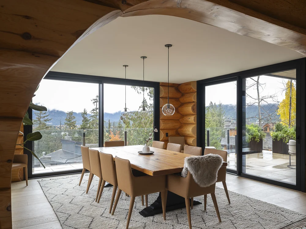 Dining table and chairs framed by a curved log arch, glazing on two sides