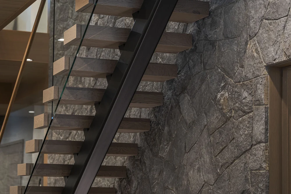 Open stair treads on a black stringer against a wall of rough stone