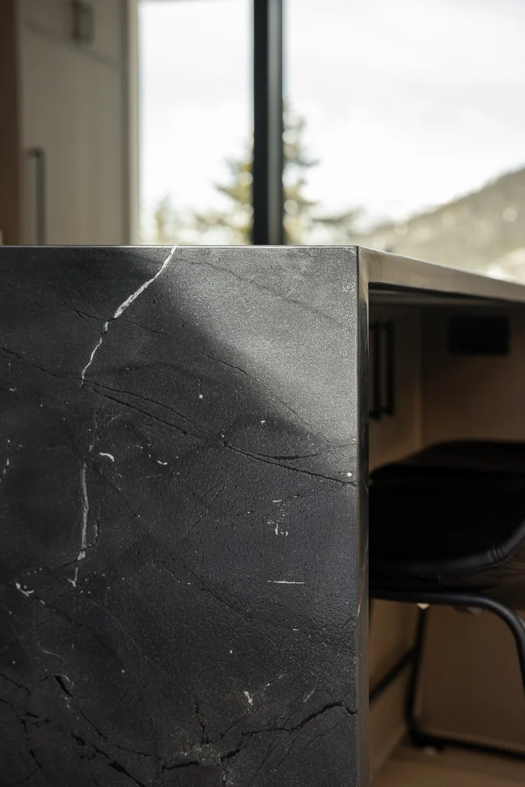Close view of a dark veined stone island end with a black stool behind it
