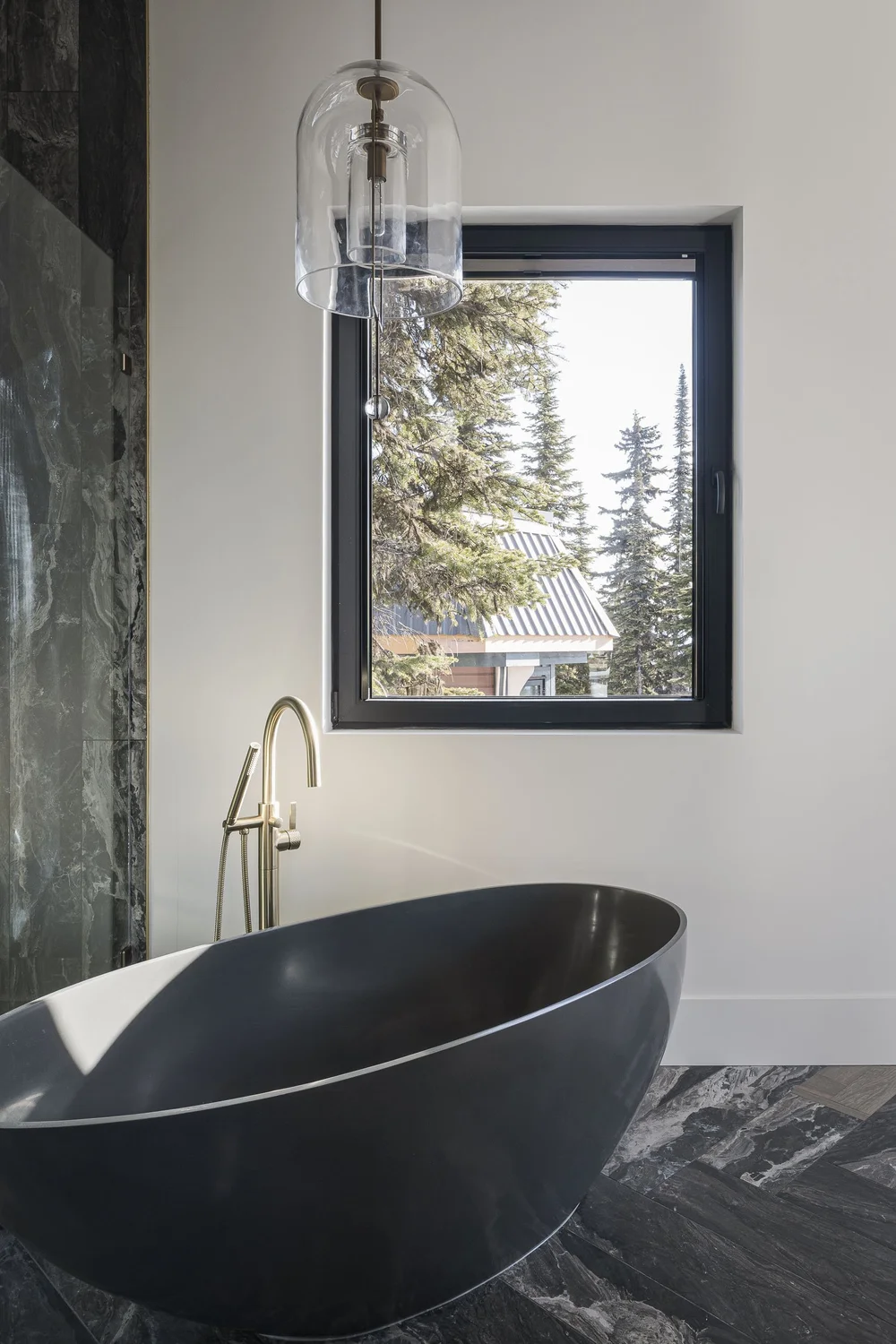Dark freestanding tub under a small window, a gold toned floor filler beside it