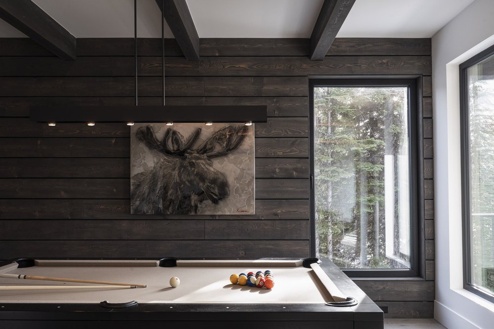 Pool table under a linear pendant, an artwork of a moose on the wood wall