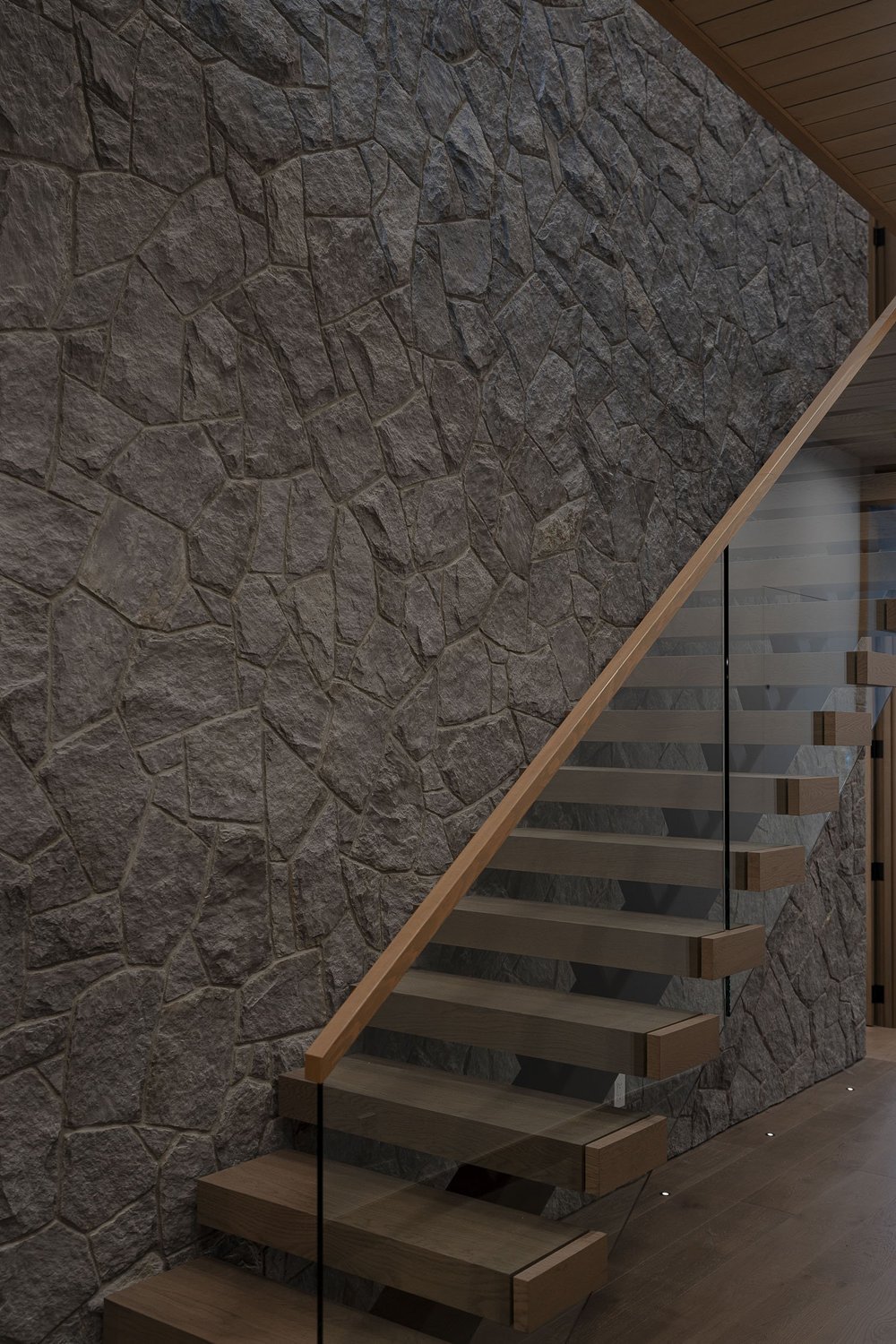 Stair rising beside a rough stone wall, glass balustrade and a slim handrail
