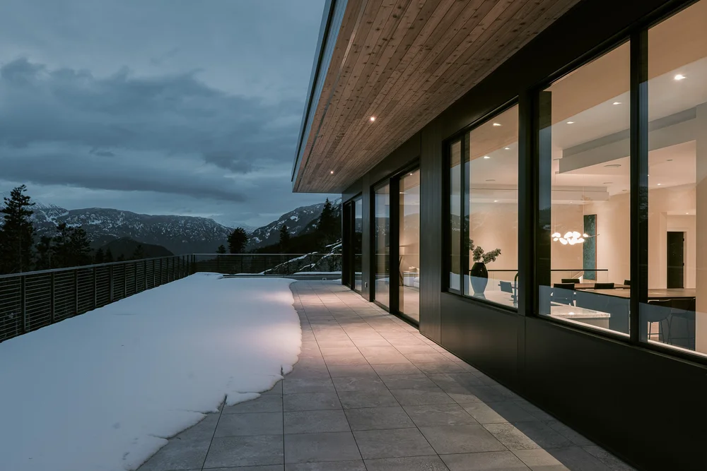 Terrace at dusk running the length of the lit glazing, snow underfoot and the valley beyond