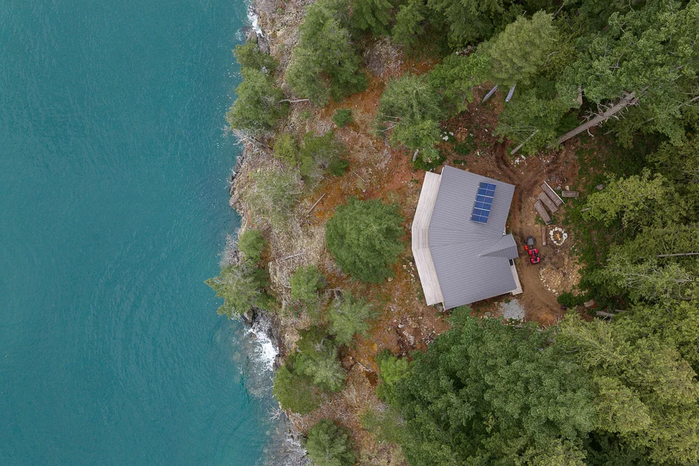 Straight down over the roof and its solar panels, rock and turquoise water alongside