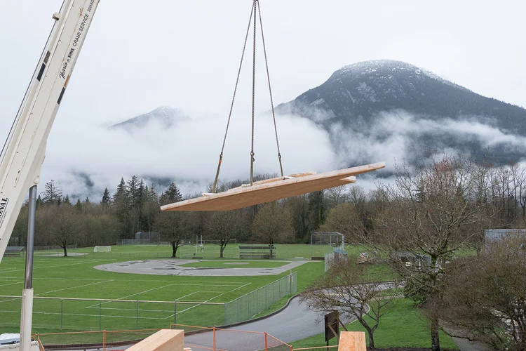 Crane lifting a CLT panel with mountain and fog behind