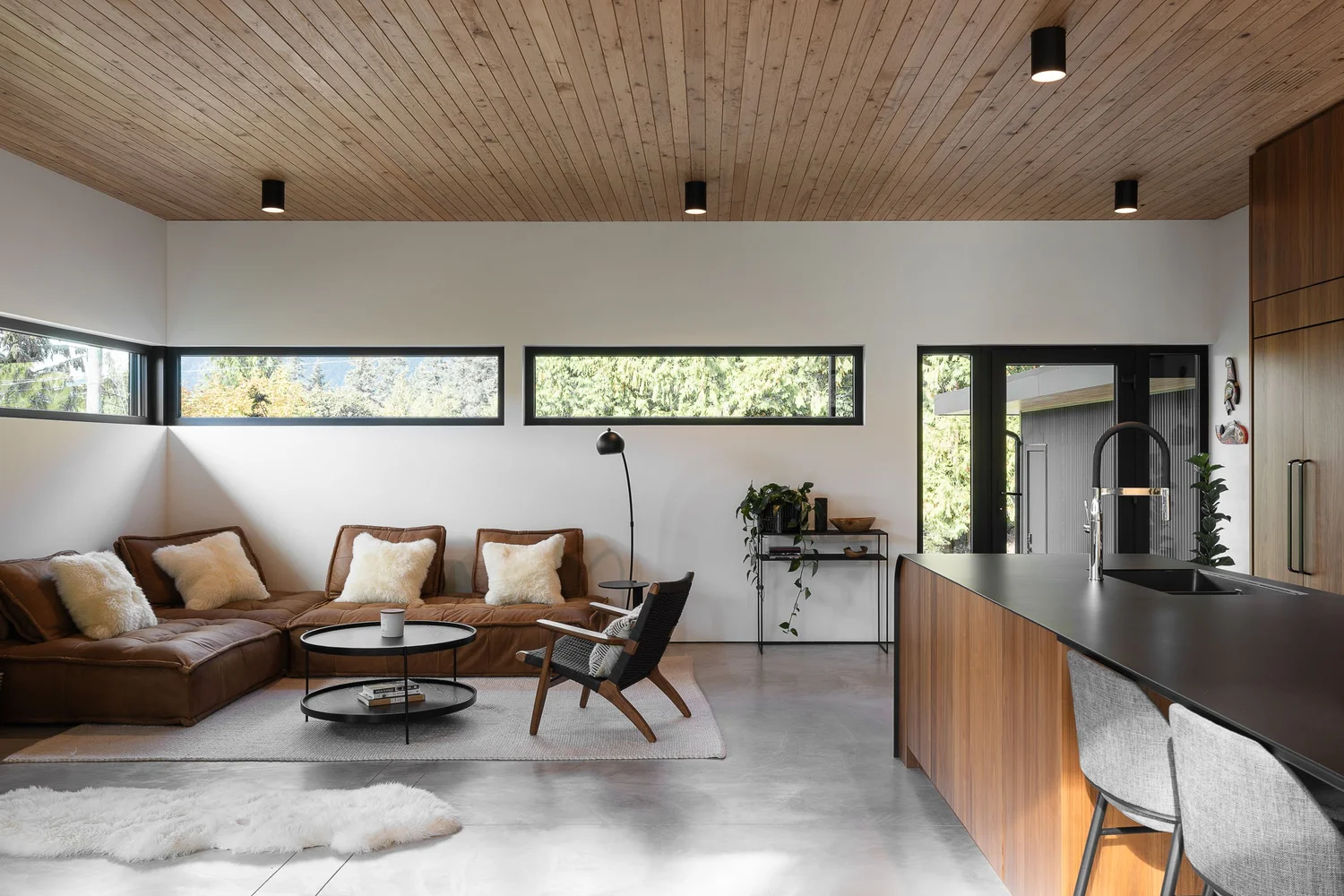 Brown leather sectional under a wood plank ceiling, clerestory windows above and the kitchen island at right