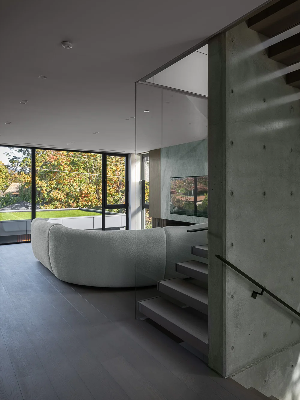 Curved sofa in front of the concrete wall, stair treads climbing past the glazing