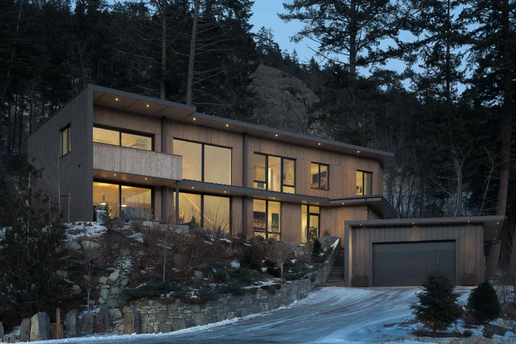 The house at twilight, warm light in every window above the driveway and the garage