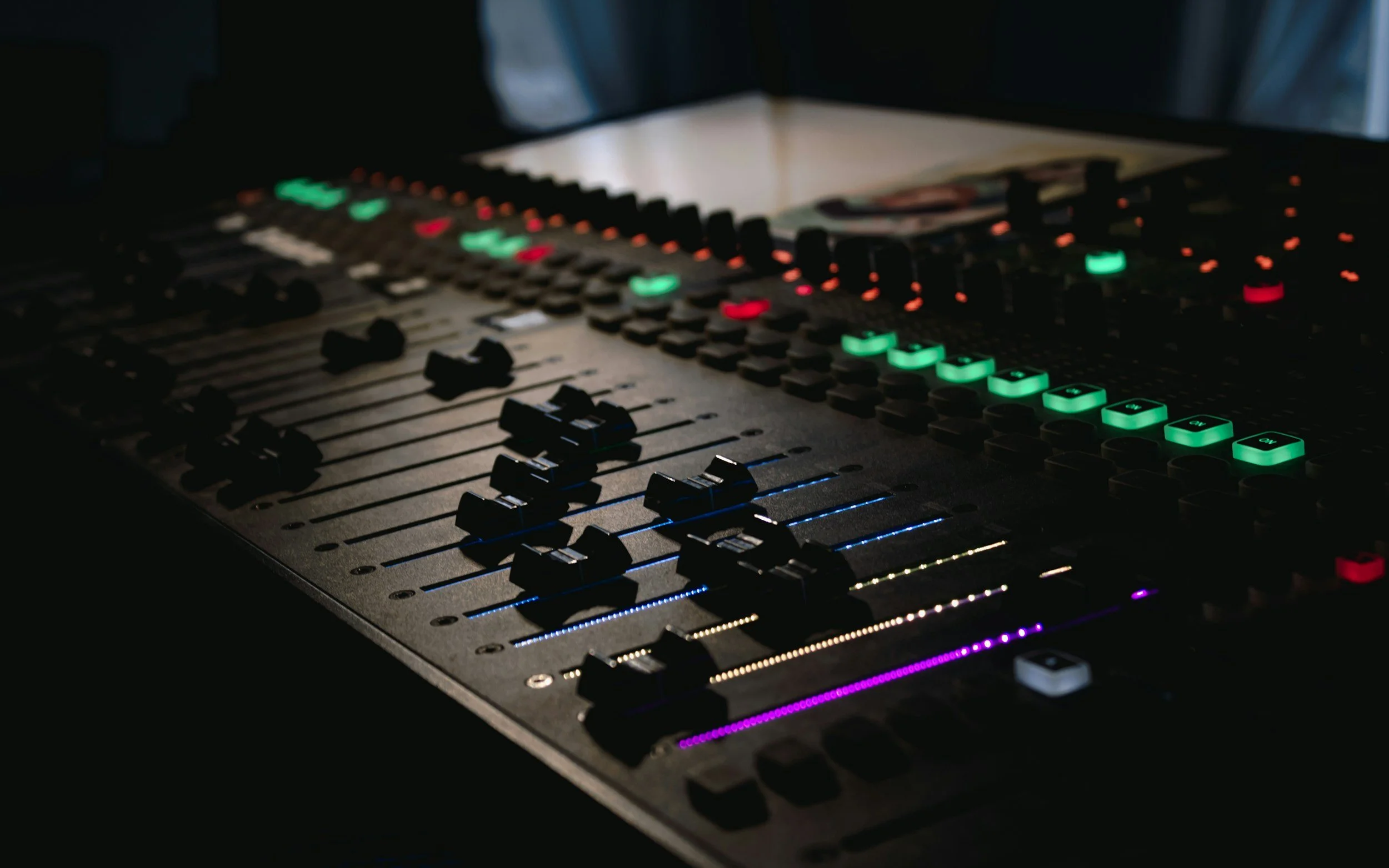 Close-up of a digital audio mixing console with illuminated faders and buttons in a dark environment.