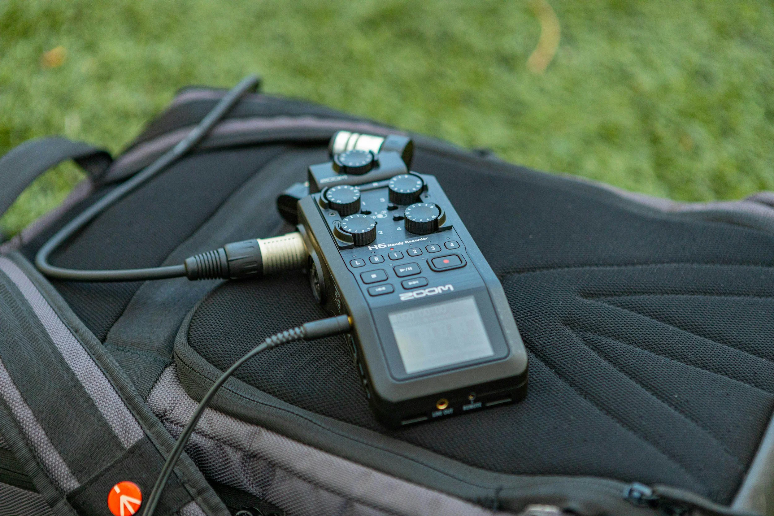Audio recording device placed on a black backpack with green grass in the background.