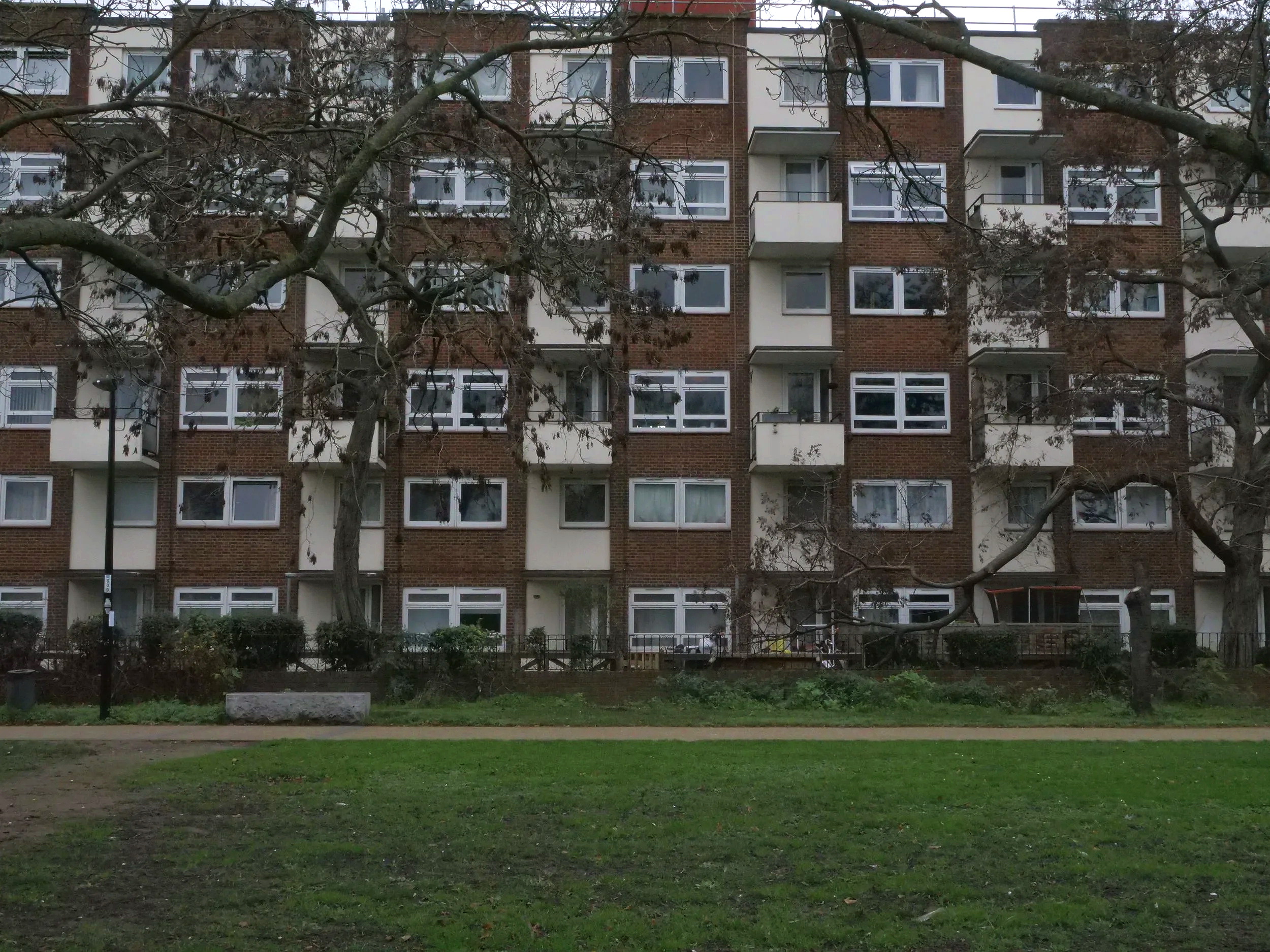 View of a multi-story brick apartment building with a grassy area and trees in the foreground.