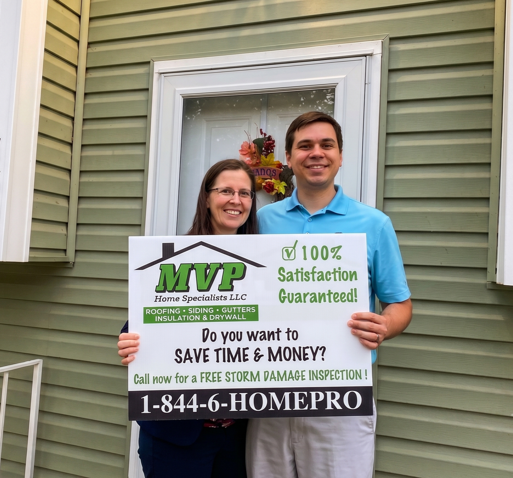 A smiling man and woman standing outside in front of a house holding a sign for MVP Home Specialists / MVP Roof Pros including roof, siding, and guttersl. The woman wears glasses and a dark top, and the man wears a blue shirt.