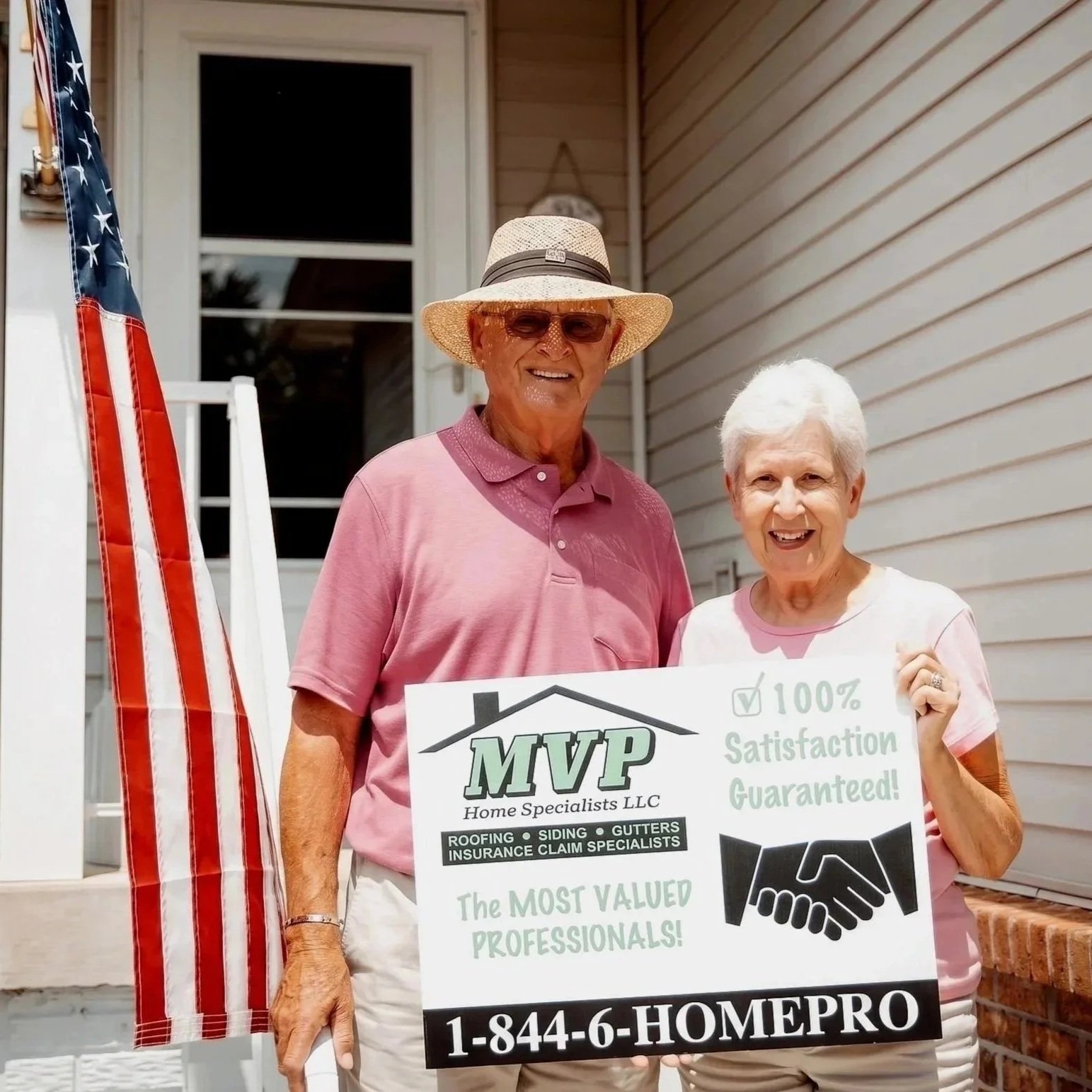 An elderly man and woman standing outside a house, holding a large sign for MVP Home Specialists / MVP Roof Pros that includes company contact information. They are smiling and dressed casually.
