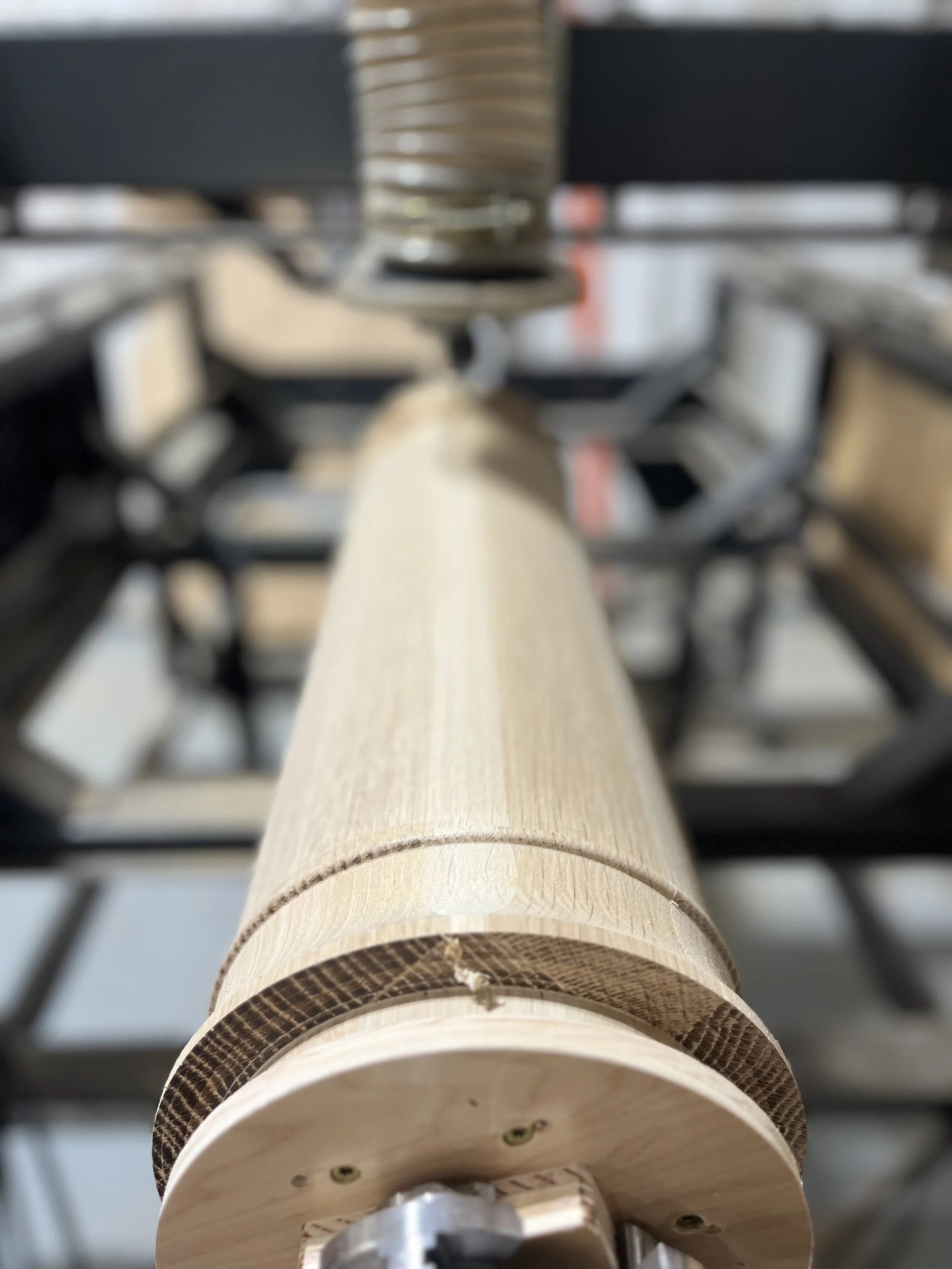 Close-up view of a wooden cylindrical object mounted on a metal apparatus, with a blurry background of workshop or manufacturing setting.