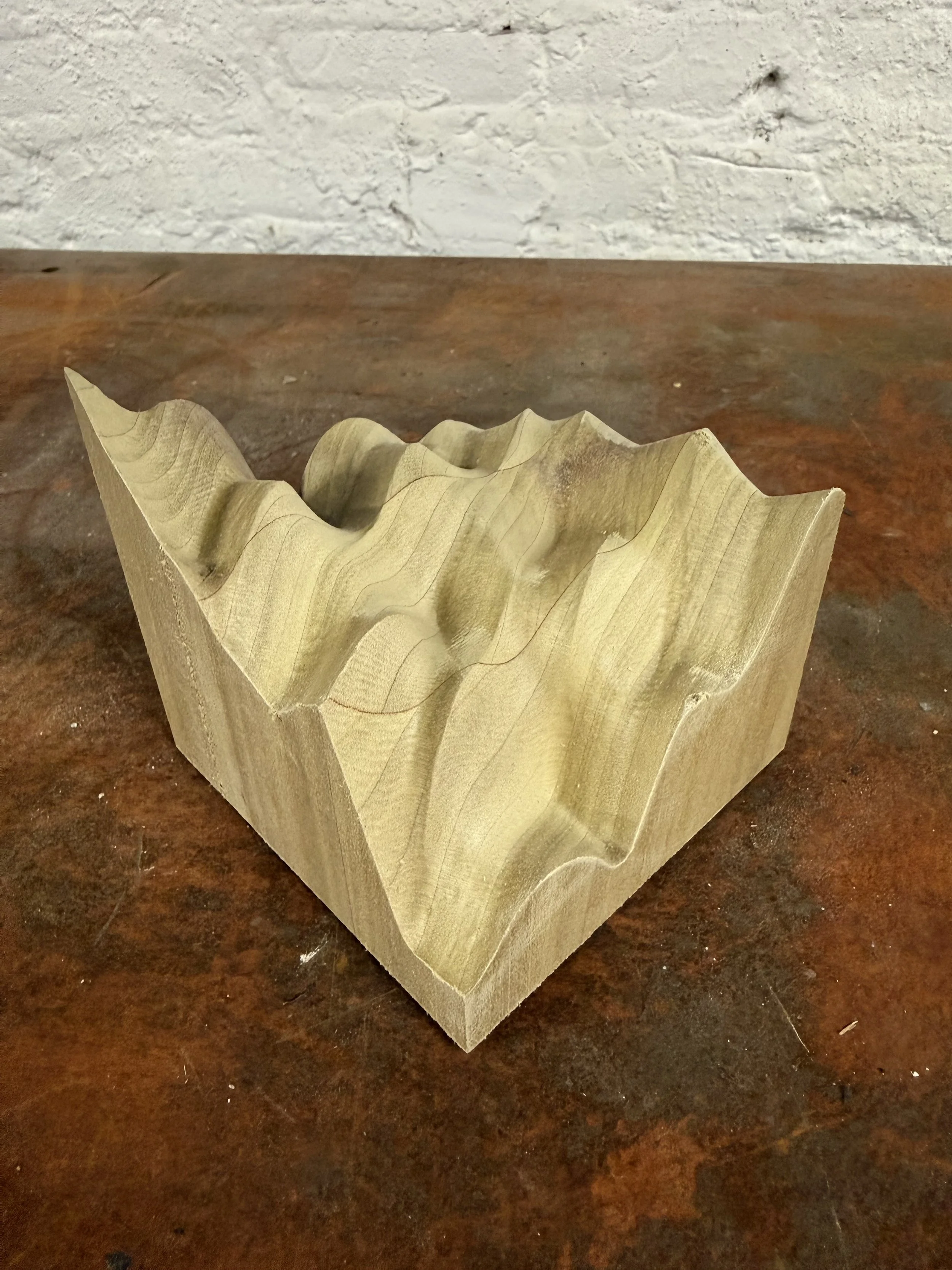 A wooden block with carved, uneven, wavy grooves on the top surface, placed on a reddish-brown wooden table.
