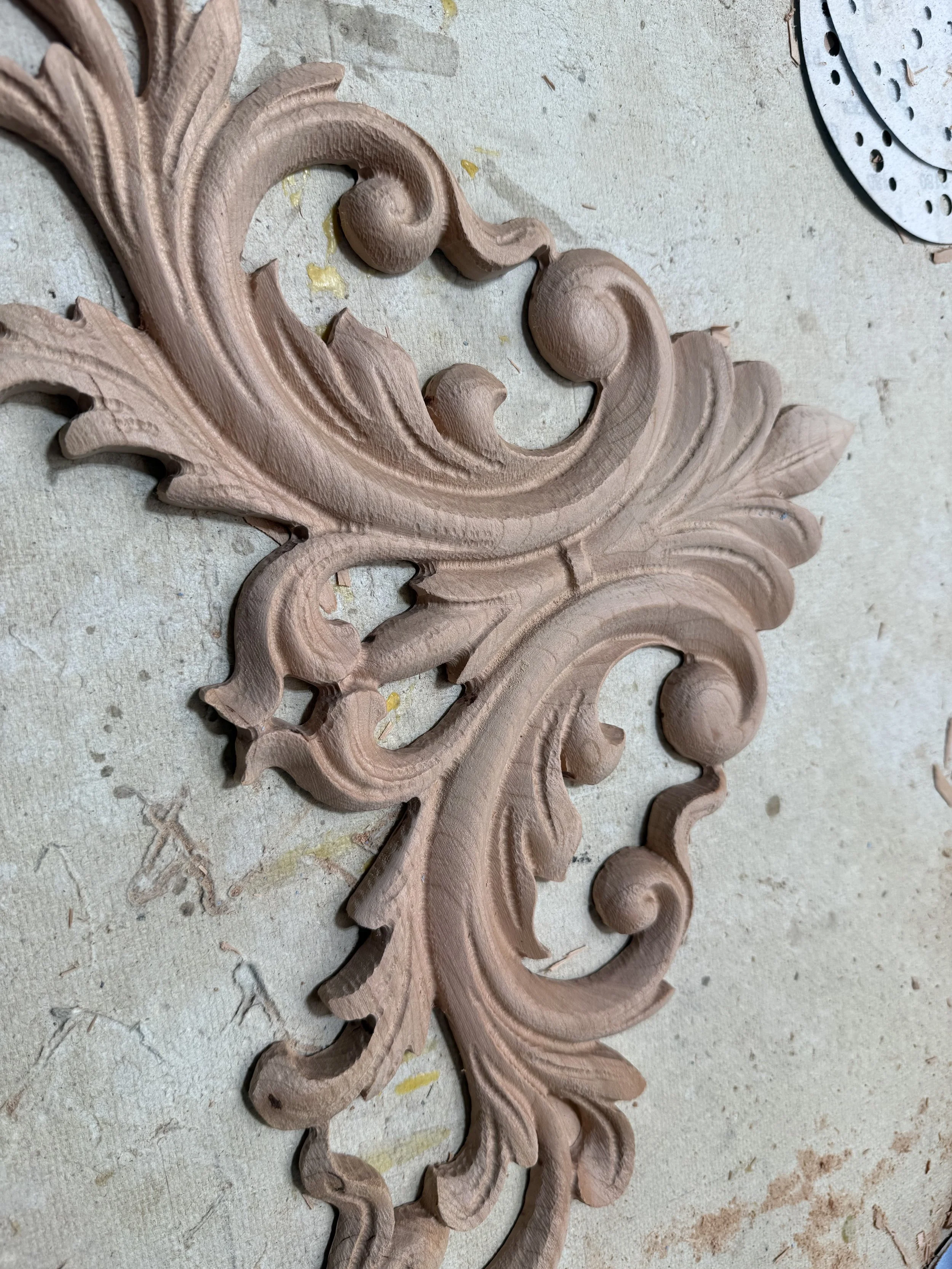 Wooden decorative carving with intricate scroll and leaf patterns on a worktable.