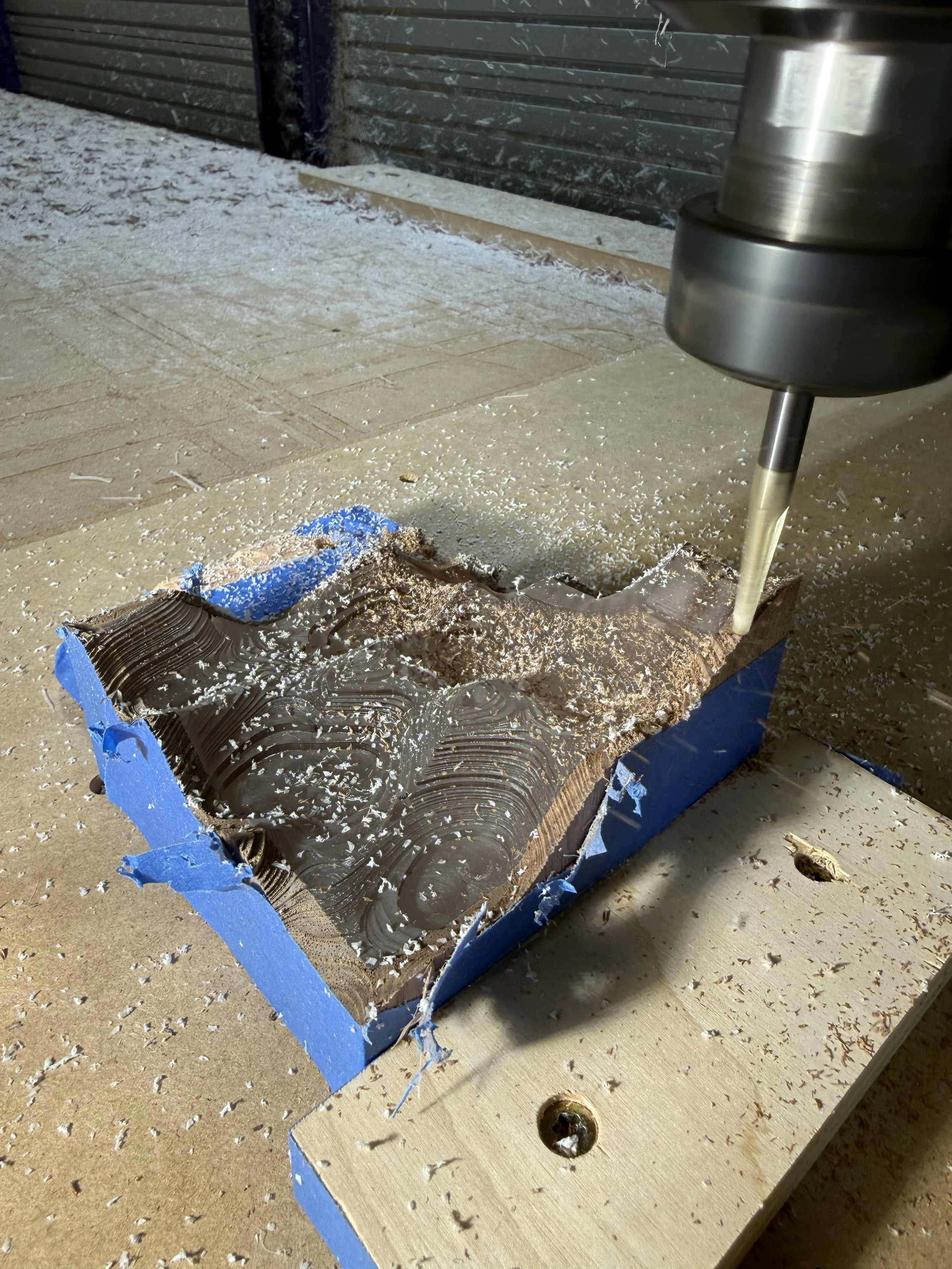 A woodworking router cutting into a piece of wood with a layer of black epoxy and wood grain patterns, in a workshop setting.