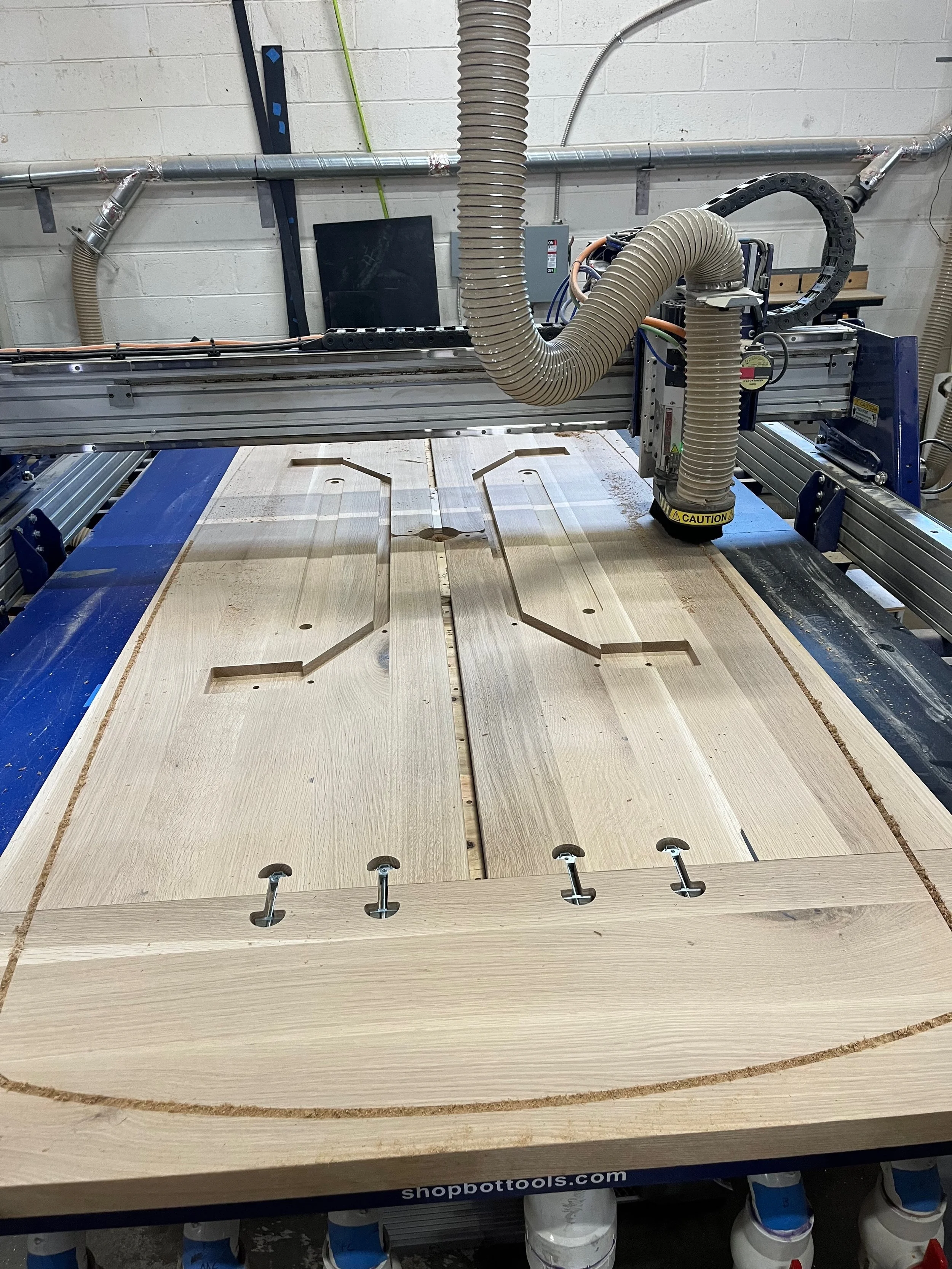 A CNC woodworking machine cutting a wooden board with intricate shapes and slots.