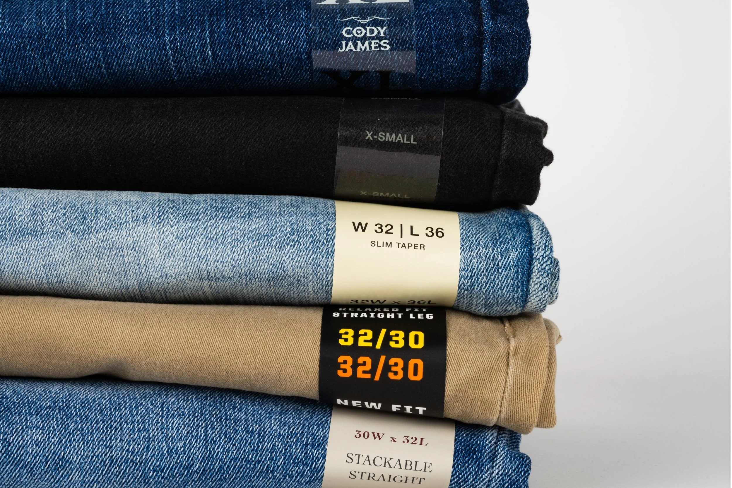 Stacked folded pants with various labels showing different sizes and styles, including denim and khaki.