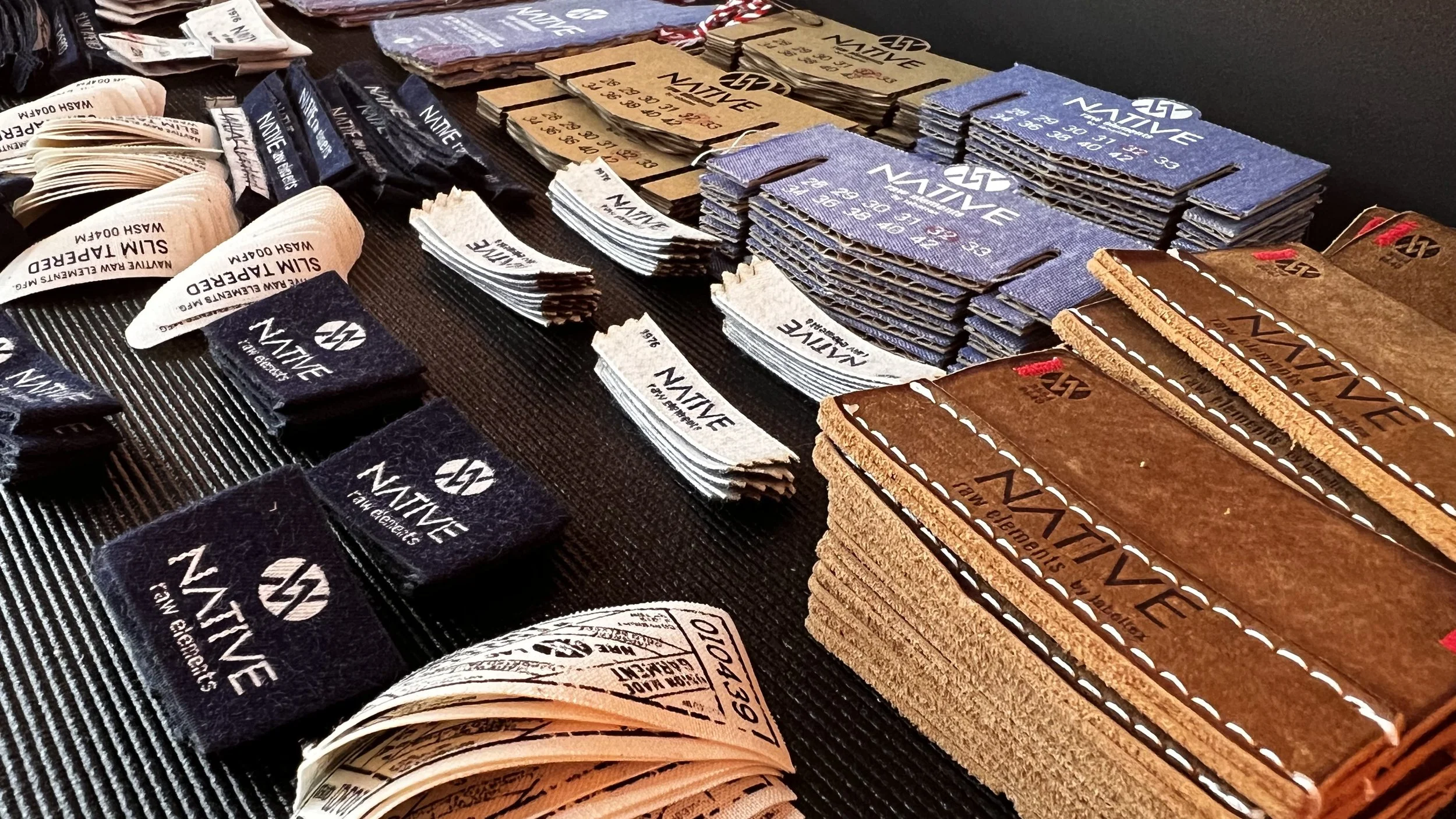 Display of various fabric samples and swatches with logos and text, including leather, denim, and other textile materials arranged on a table.