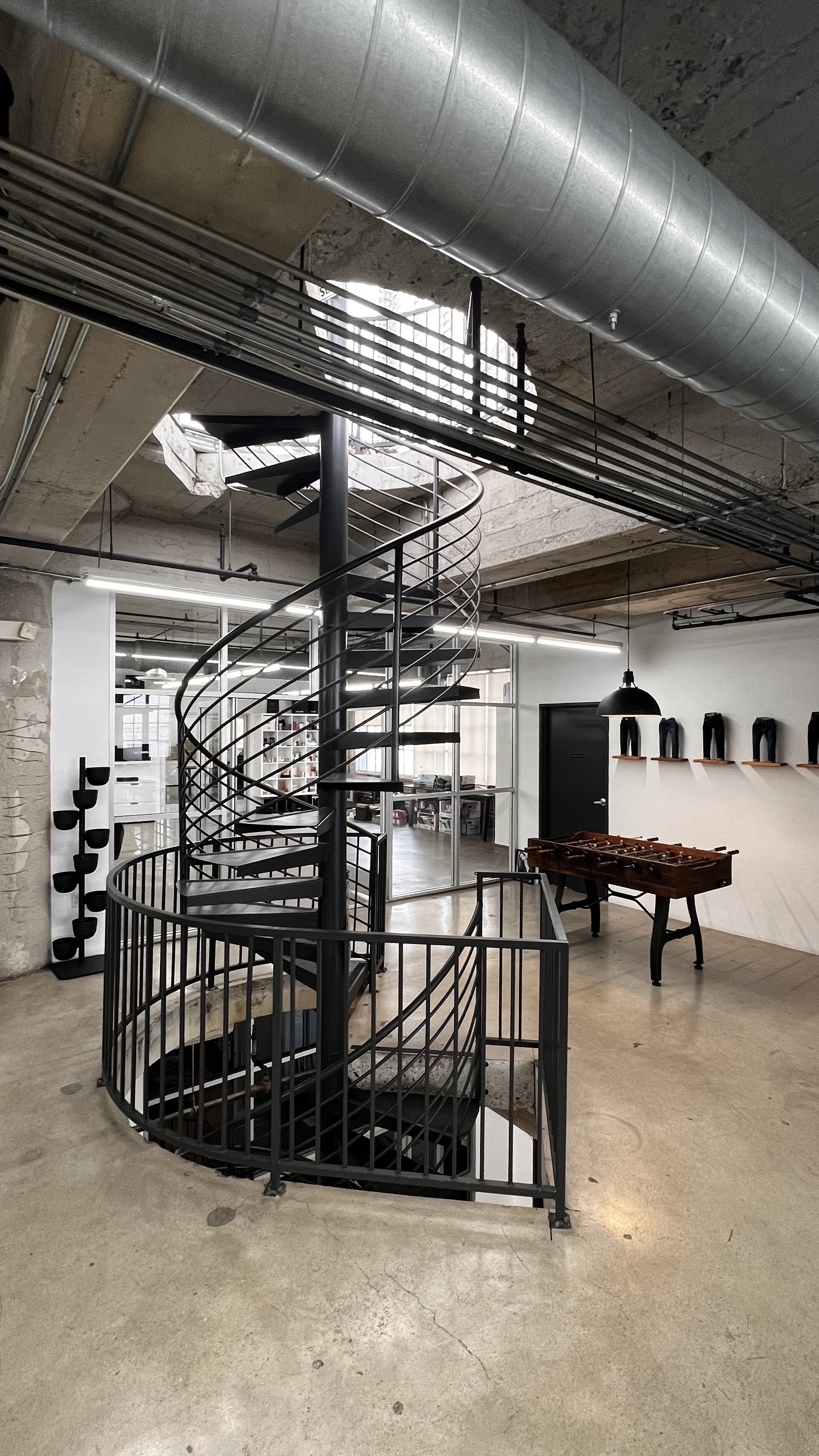 Indoor industrial-style space with a black spiral staircase, foosball table, and wall-mounted shelves with different shaped objects.