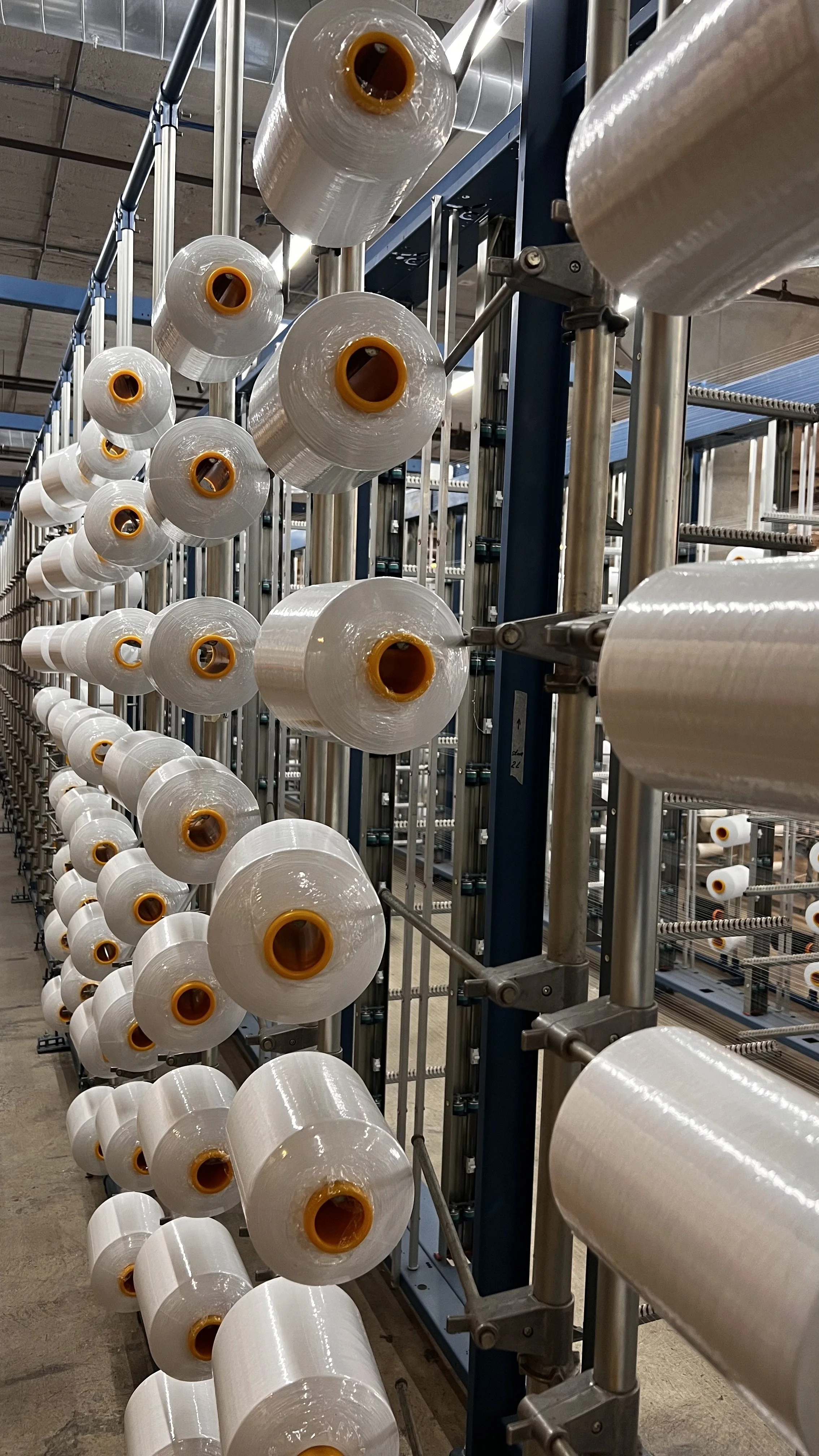 Rows of large white spools of plastic filament on a manufacturing line.
