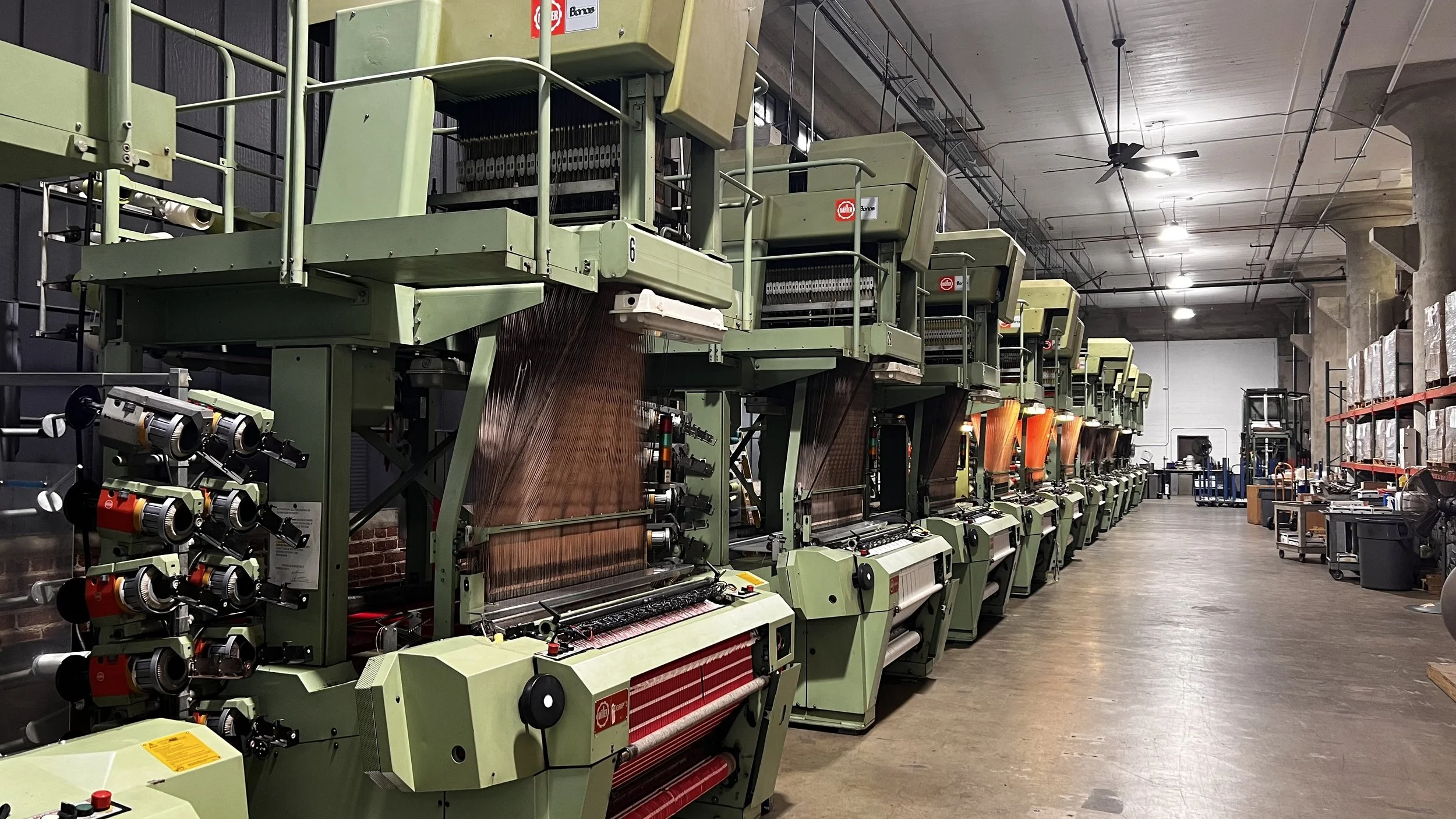 Row of industrial textile weaving machines in a factory.