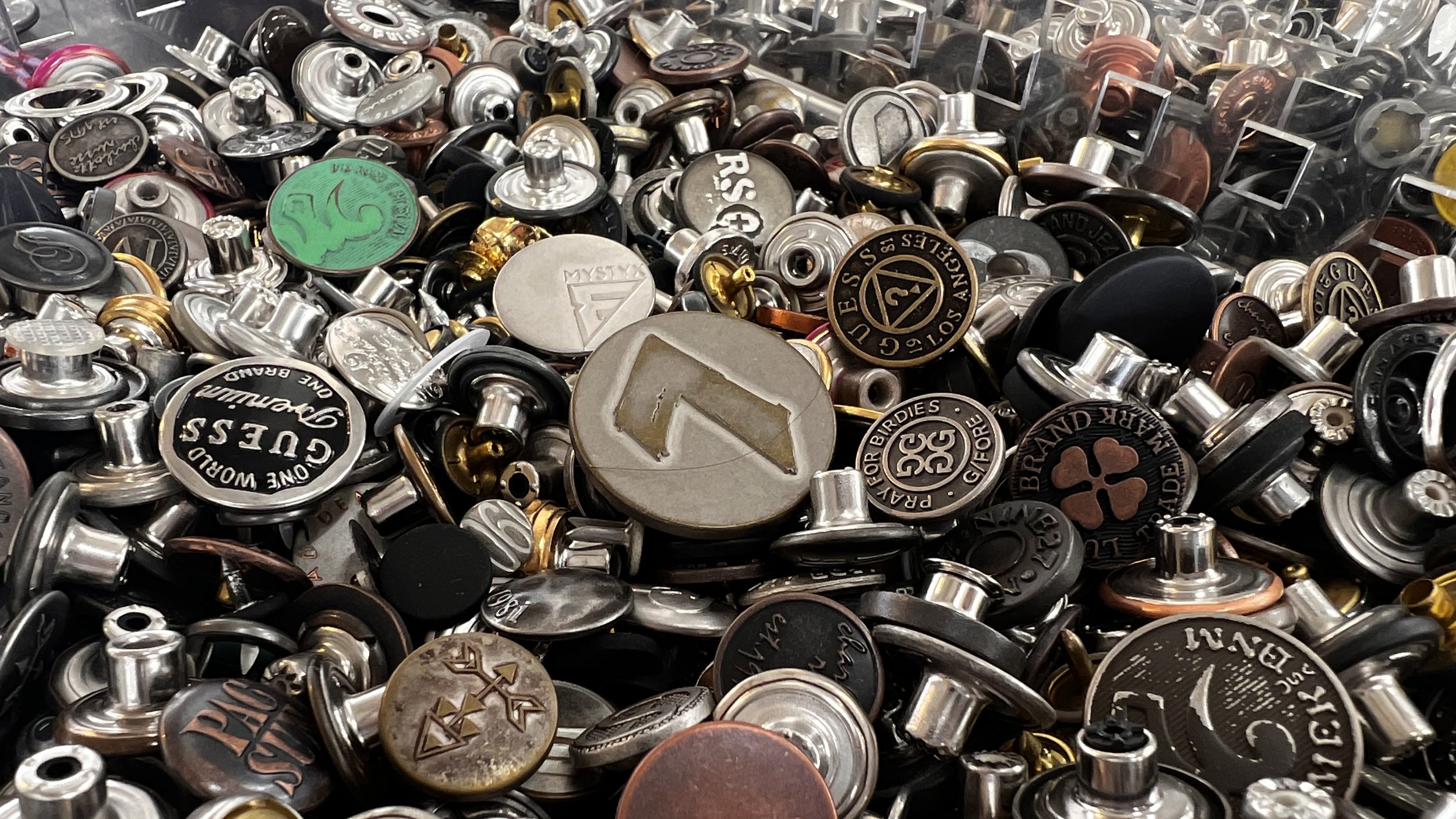 A large pile of golf equipment markers, some with brand logos and symbols, made of metal, plastic, and assorted materials.