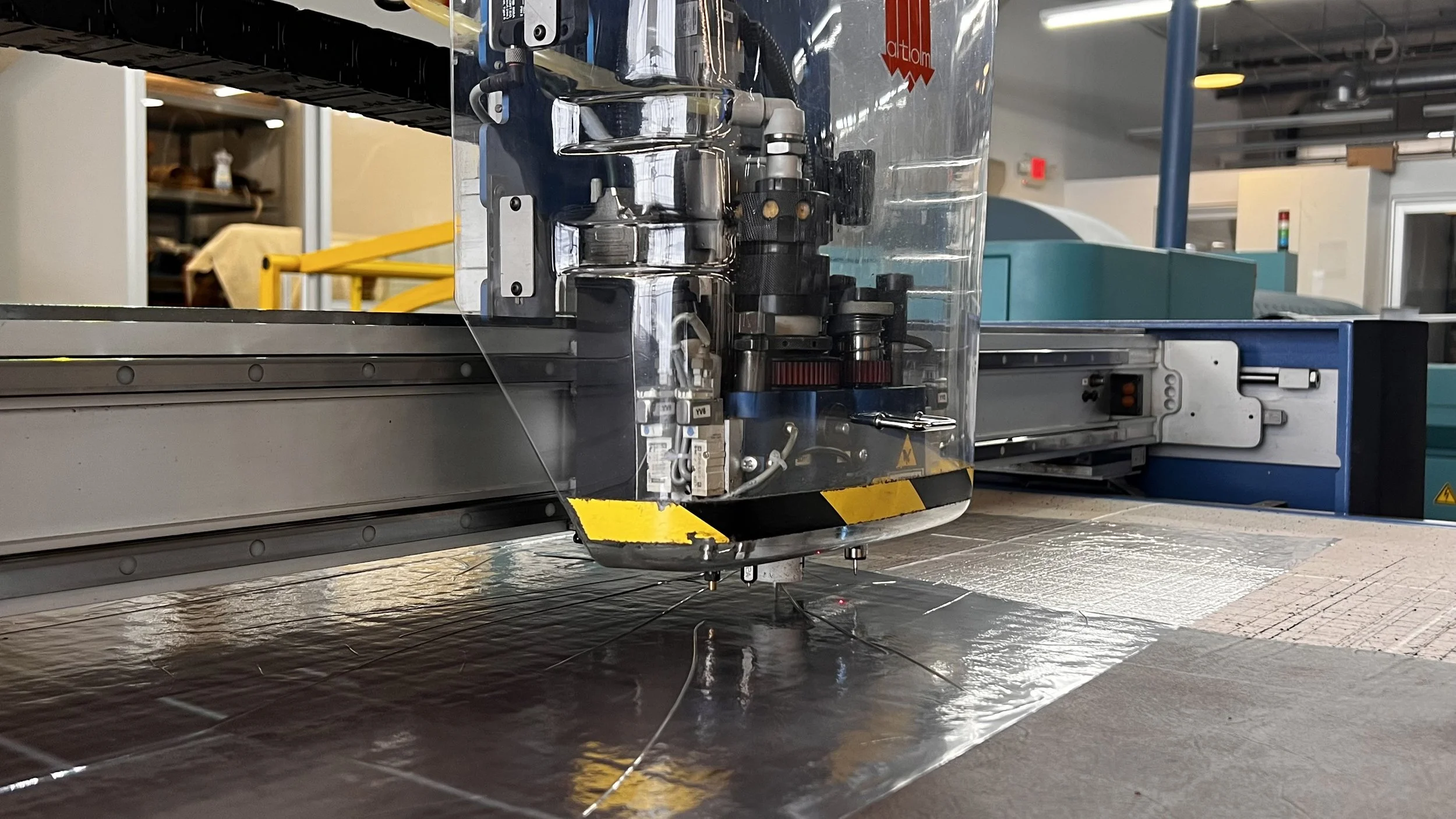 Close-up of a machine on a flat surface, with a transparent cover, wires, and mechanical parts, in a manufacturing or industrial setting.