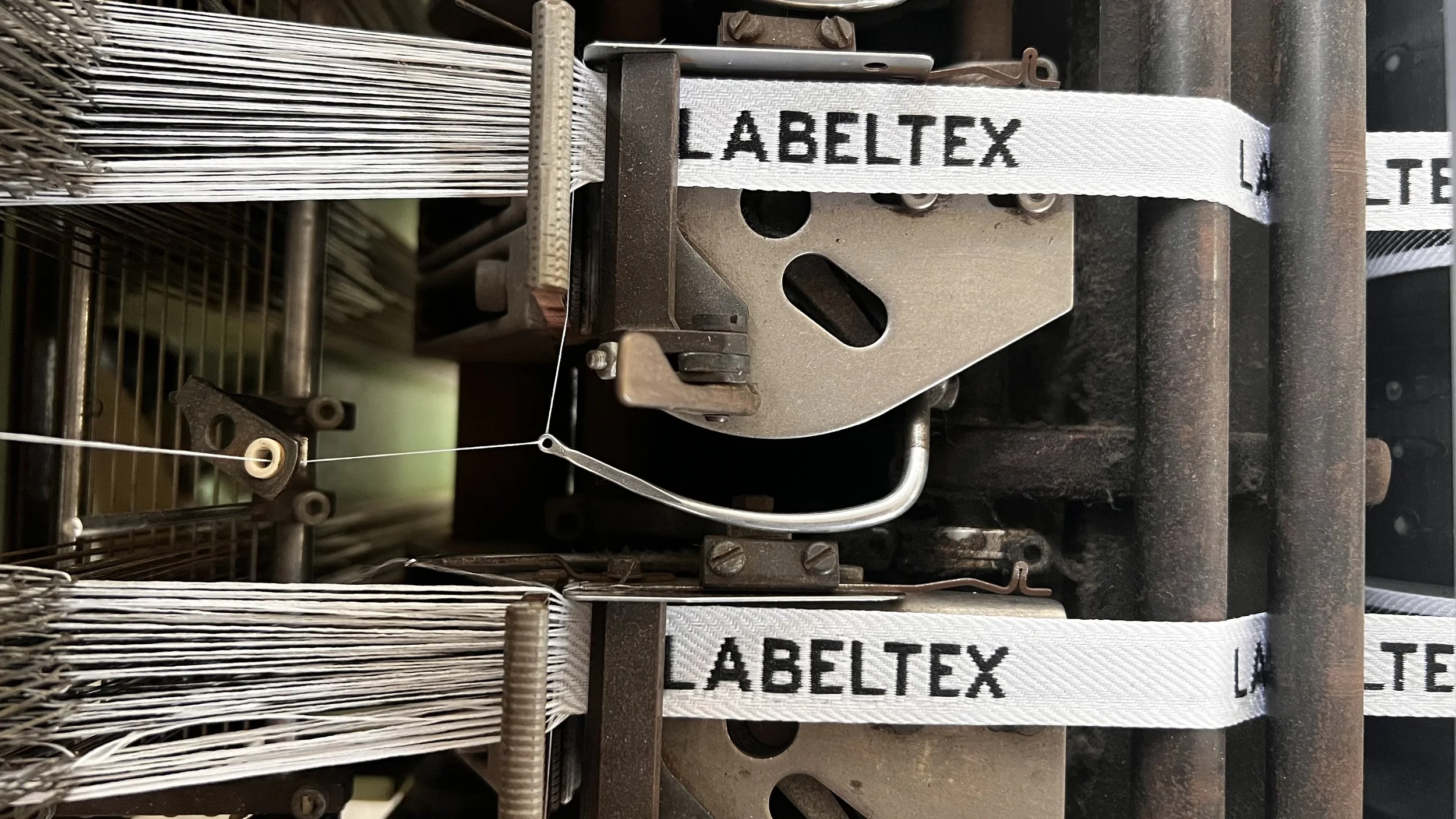 Close-up of a machine with white straps labeled 'LABELTEX', metal components, wires, and rusted parts.