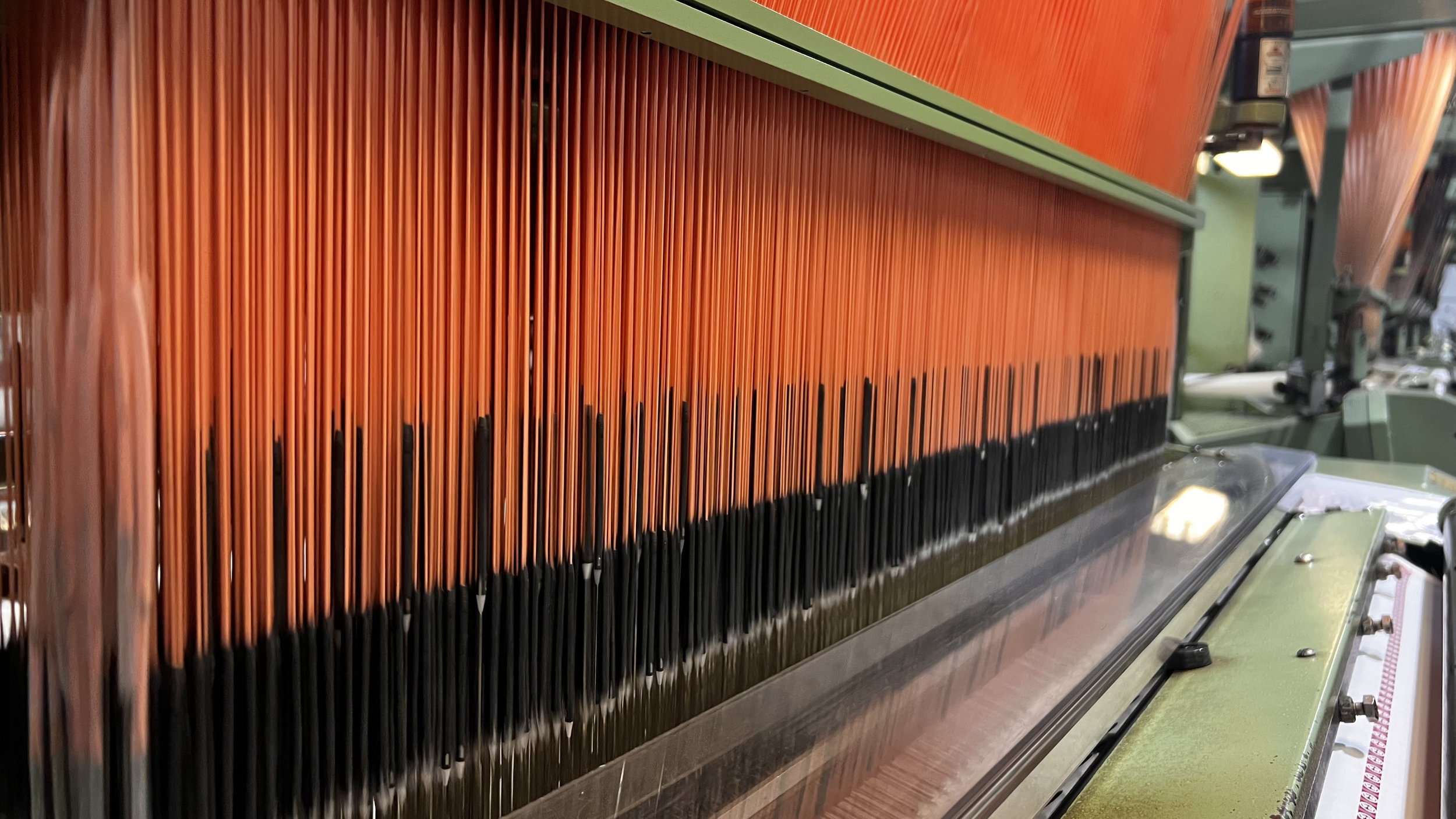Close-up of a vintage woven-instrument, possibly a musical instrument or loom, with orange and black vertical stripes and metallic components.