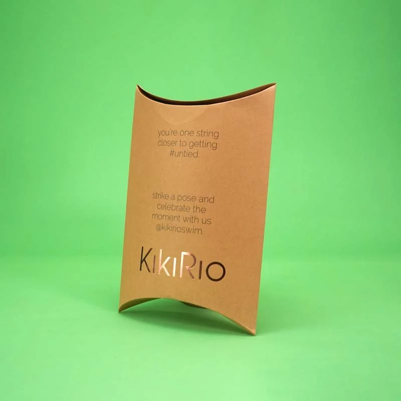 Brown paper bag with cutout letters spelling Kikirio, standing on a green background, with text about getting closer to being united and celebrating a moment.