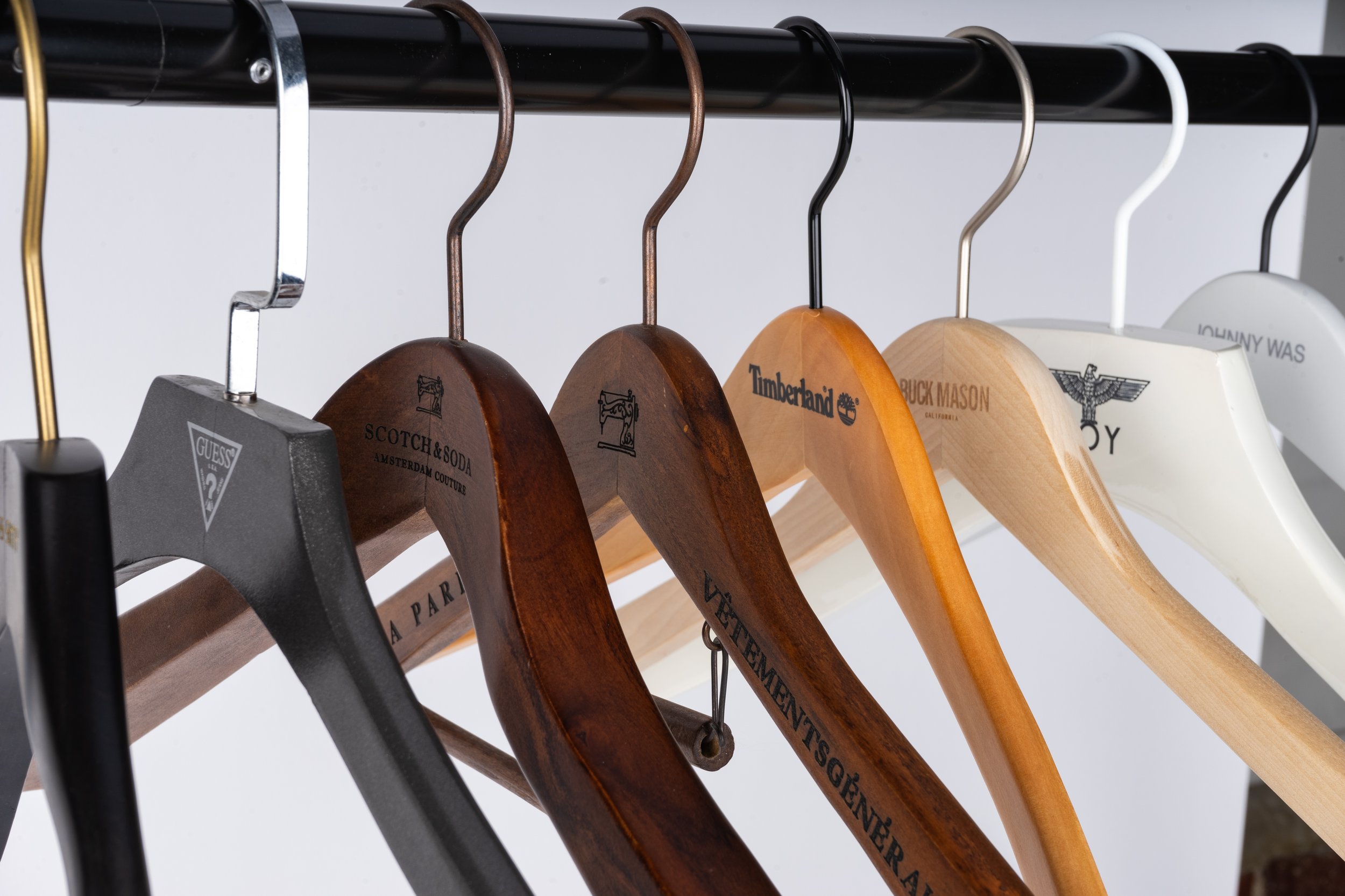 A row of empty clothing hangers on a black metal clothing rack, featuring various styles and materials, including wood, plastic, and metal.
